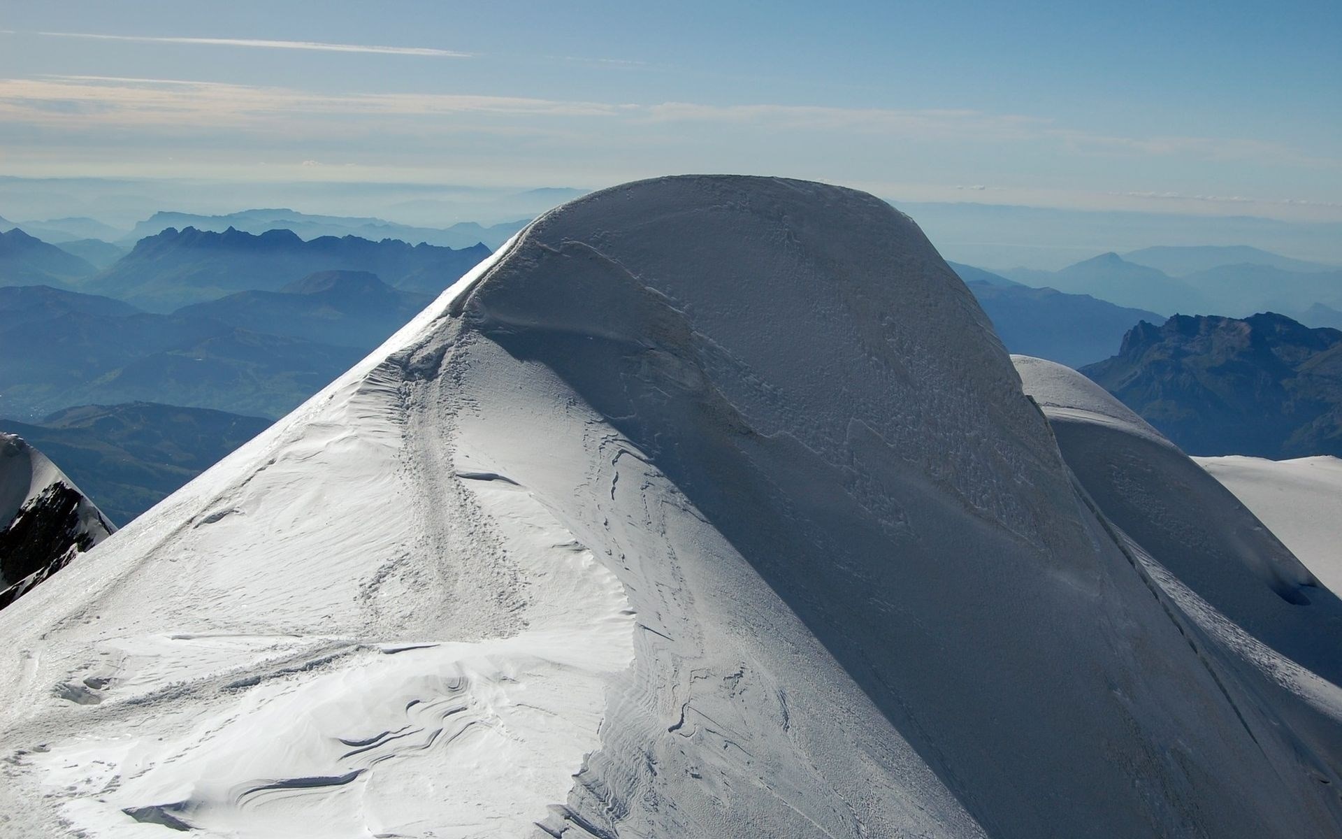 Snow-covered mountain peak with distant blue mountains HD Wallpaper