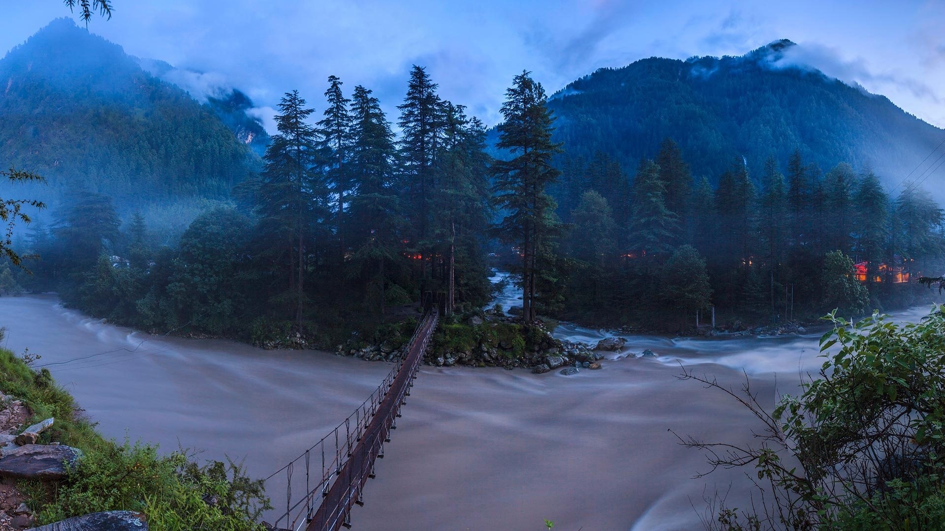 Suspension bridge over a river in a mountainous forest HD Wallpaper