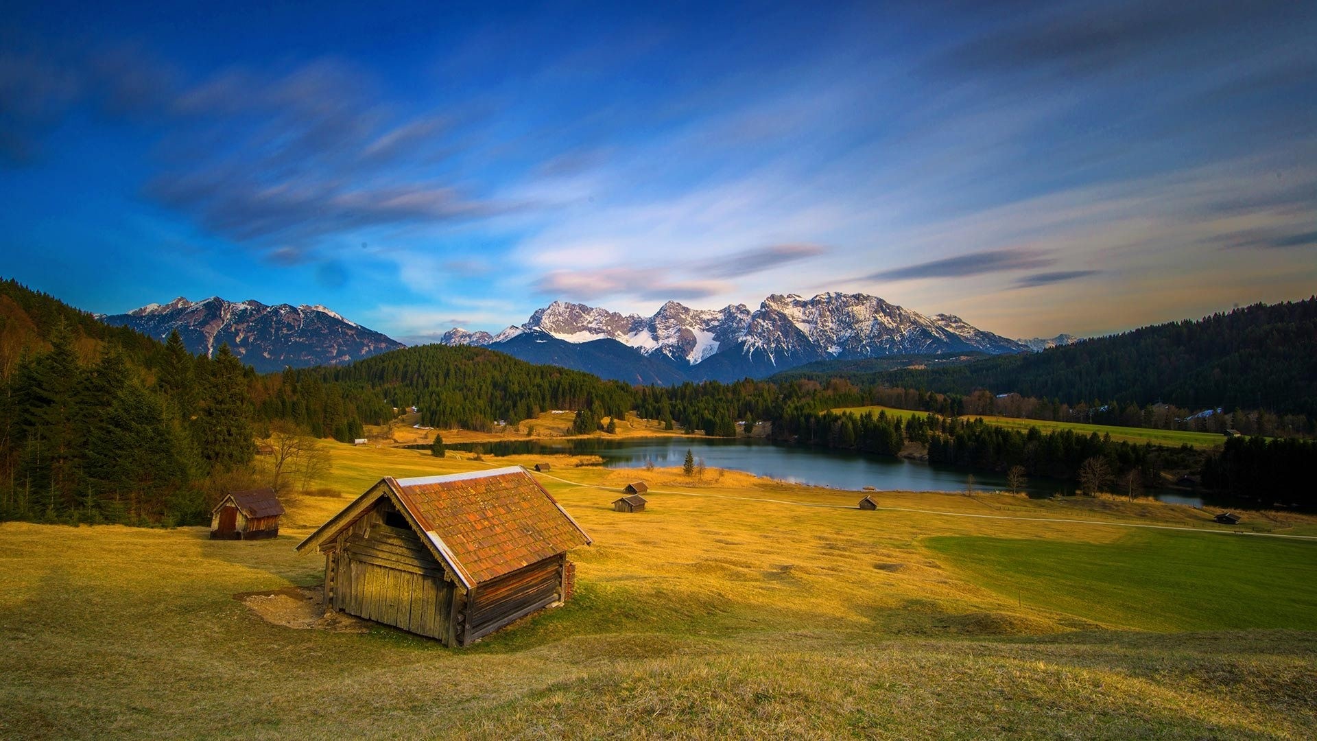 Wooden cabin by a lake with snow-capped mountains in the background HD Wallpaper