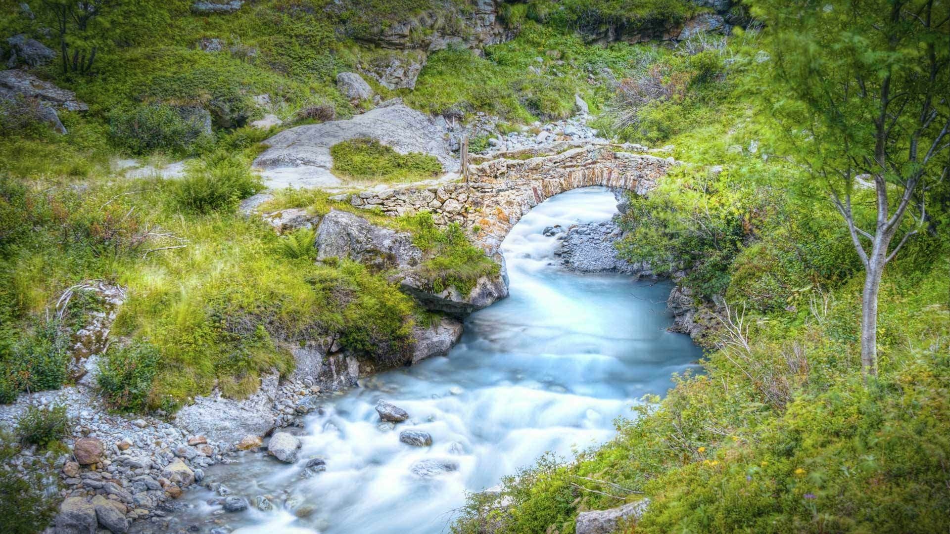 Stone bridge over a flowing river in a green landscape HD Wallpaper