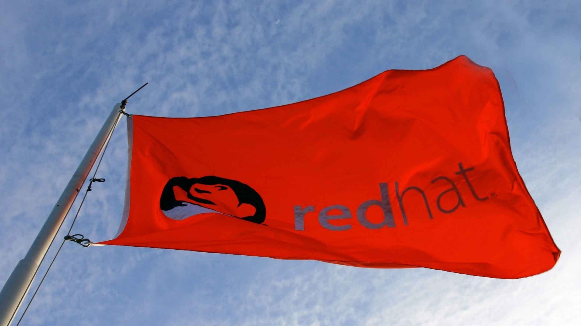 Red Hat flag waving against a blue sky HD Wallpaper