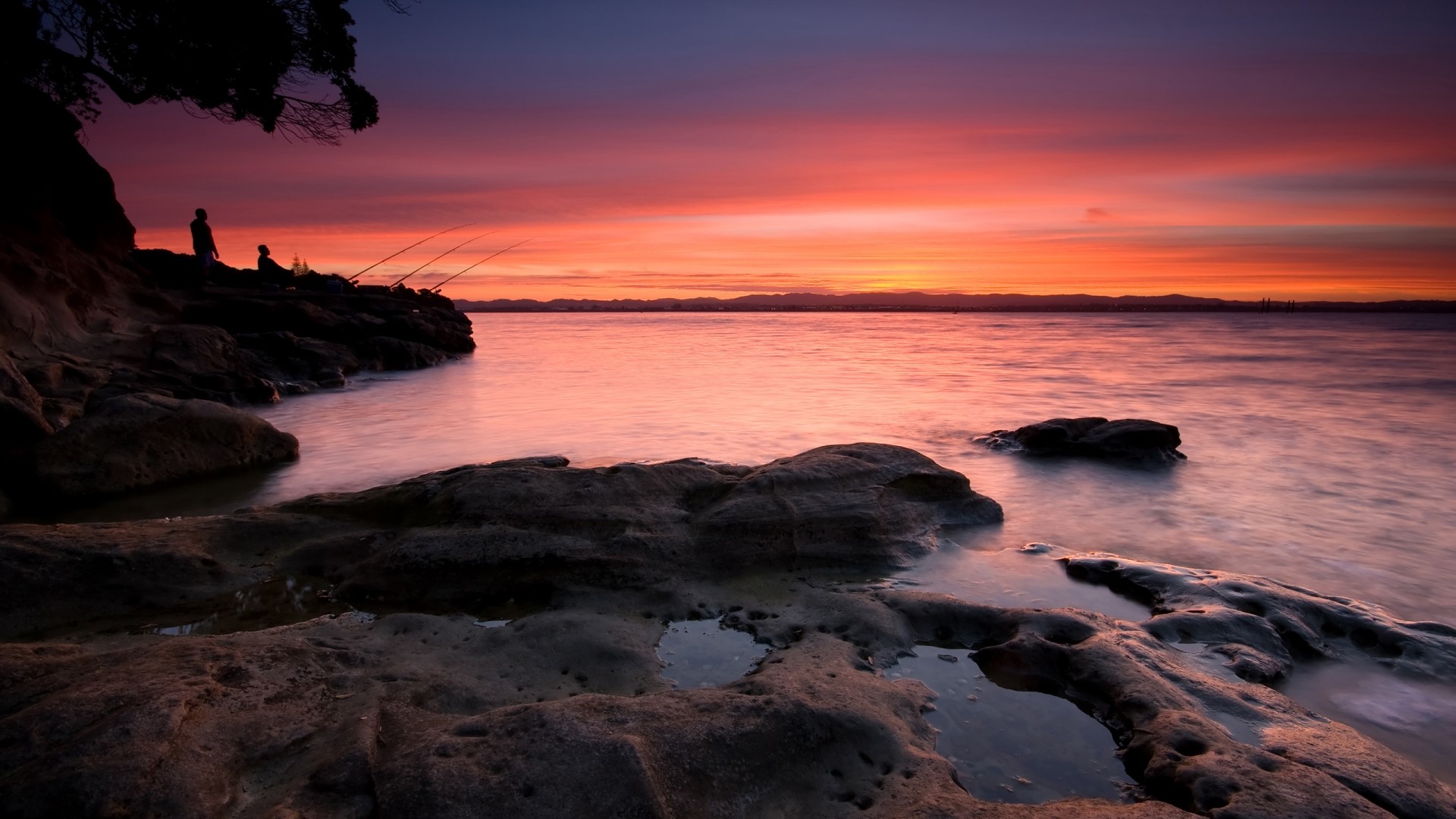People fishing at sunset on rocky shore HD Wallpaper