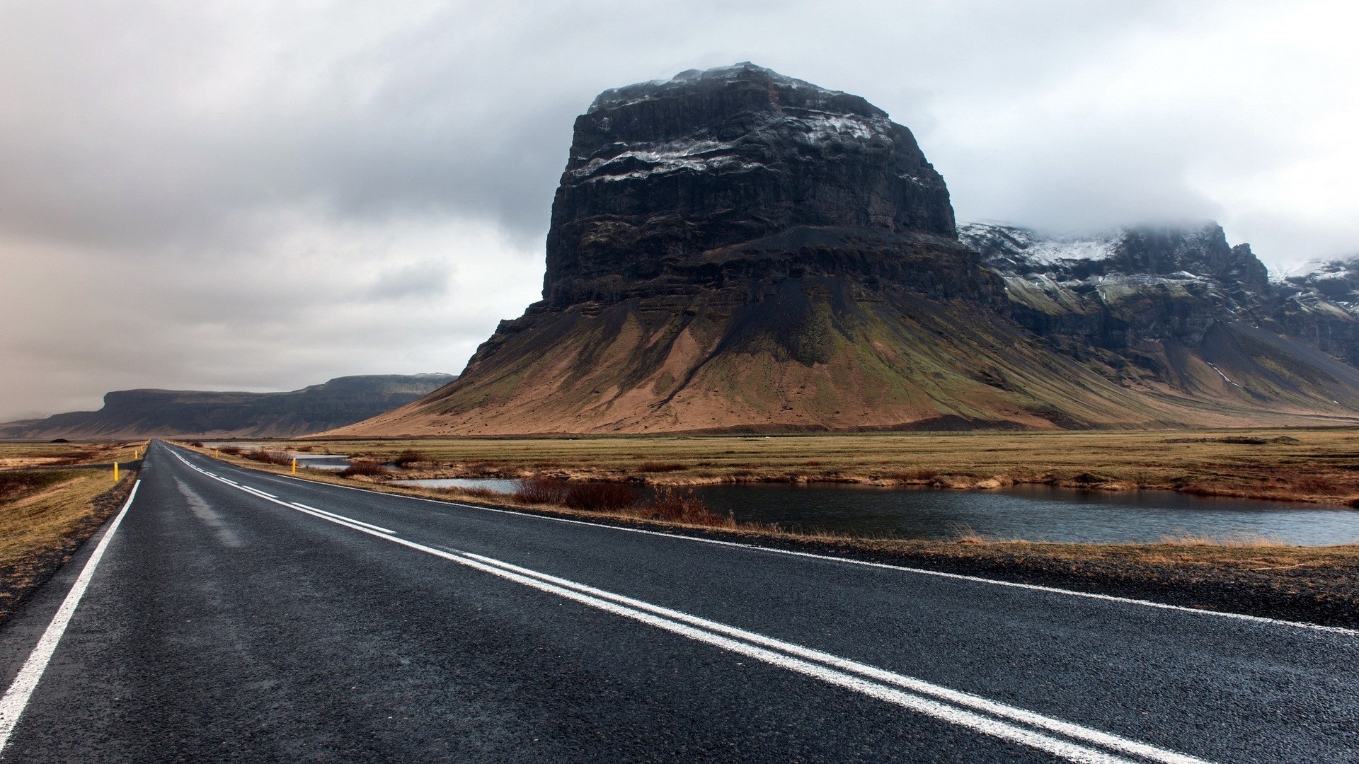 Road leading to a large mountain under a cloudy sky HD Wallpaper