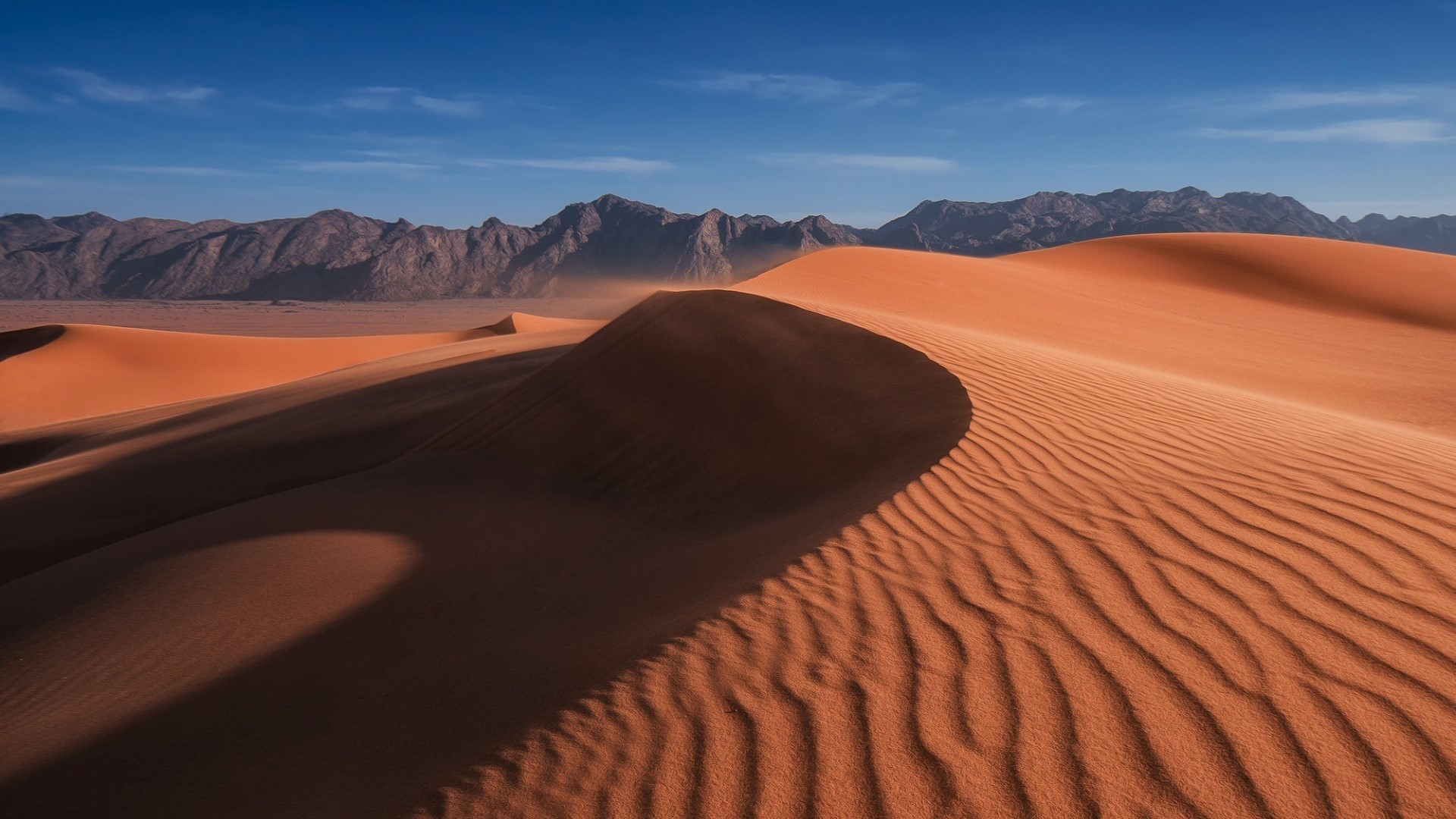 Sand dunes and desert mountains under a blue sky HD Wallpaper