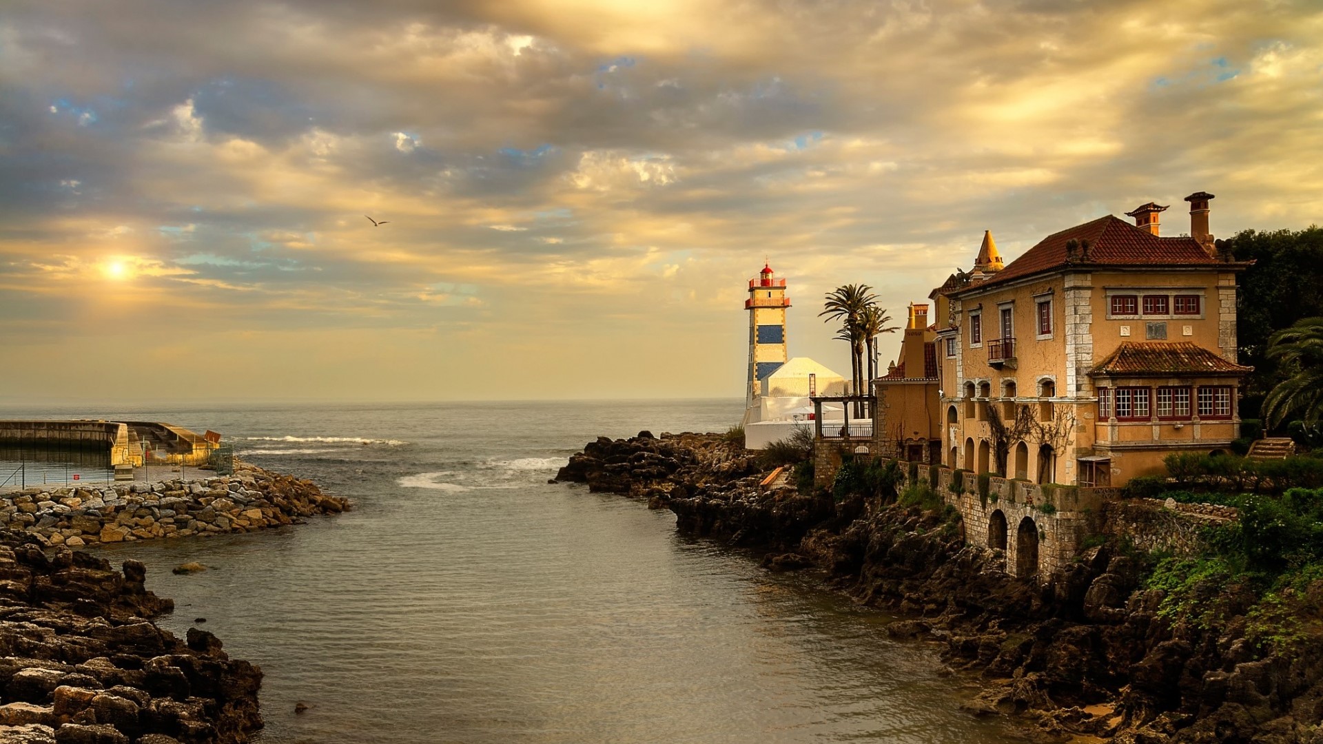 Lighthouse and mansion on rocky coast at sunset HD Wallpaper