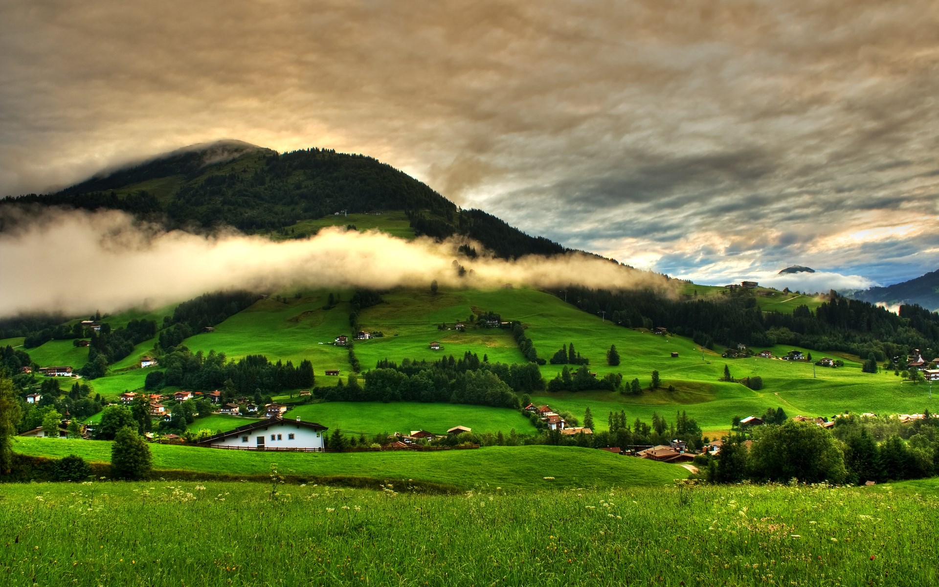 Green rolling hills with houses and clouds HD Wallpaper