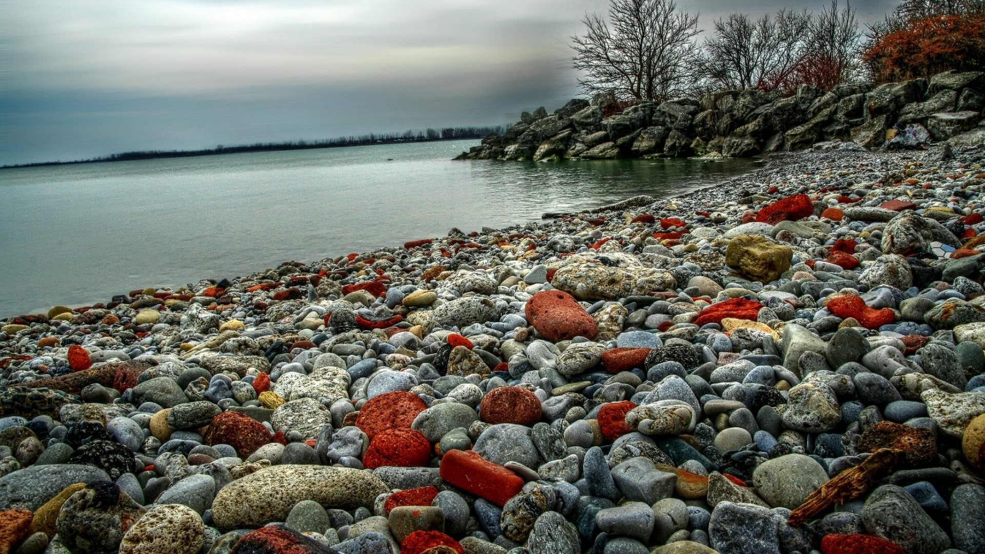 Pebble beach with calm water and rocky shore HD Wallpaper