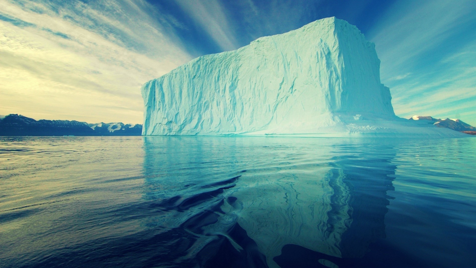 Large iceberg in the ocean with mountains in the background HD Wallpaper