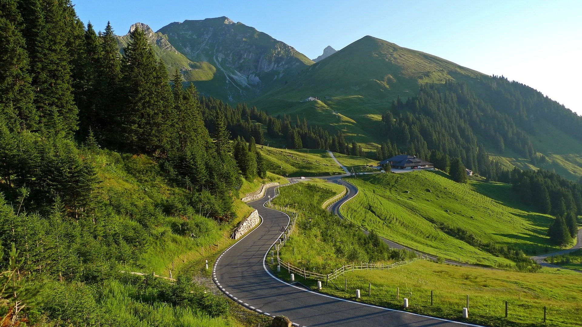 Winding mountain road through green hills and forests in Switzerland HD Wallpaper