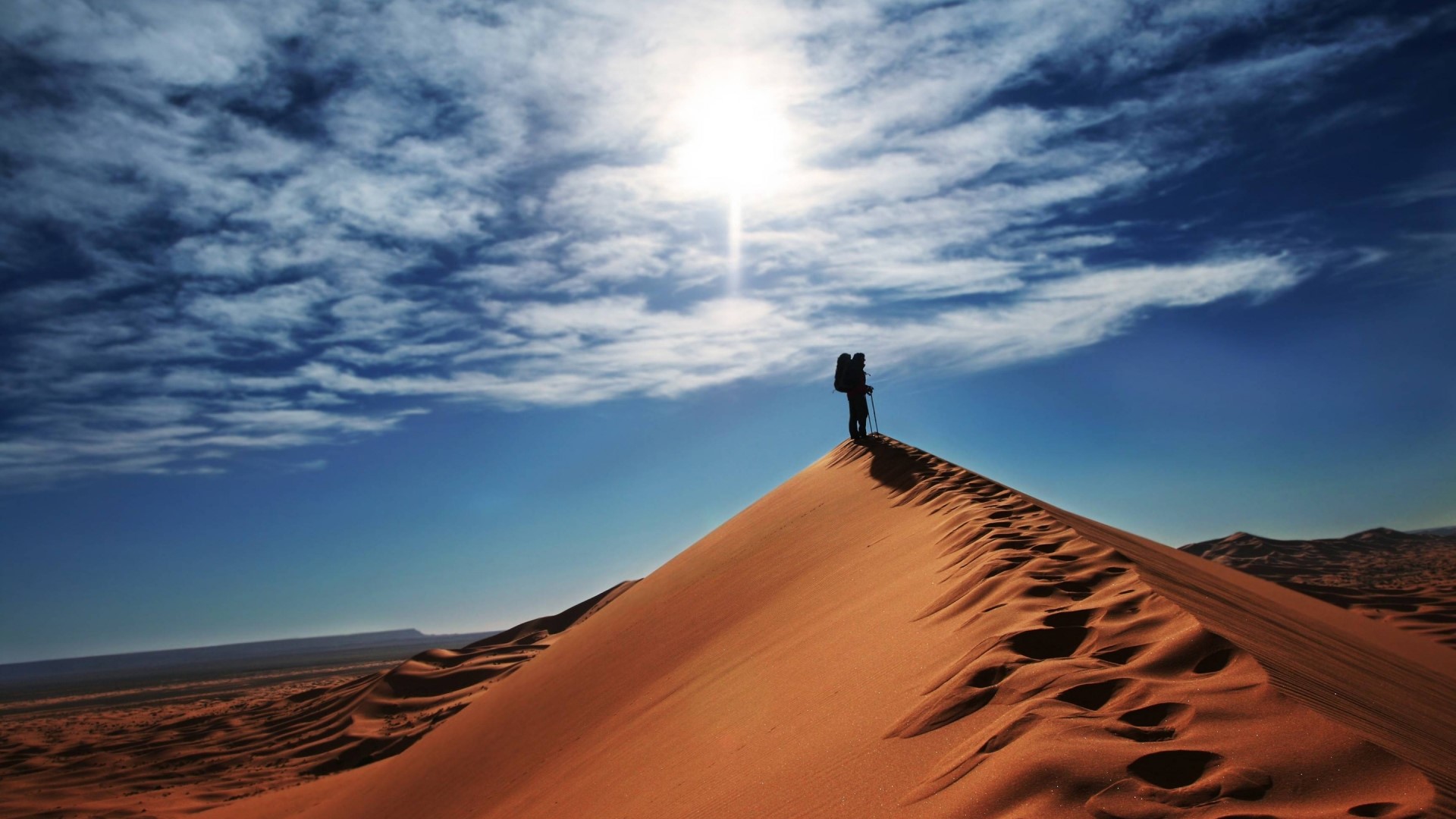 Person with backpack on desert dune under sun HD Wallpaper