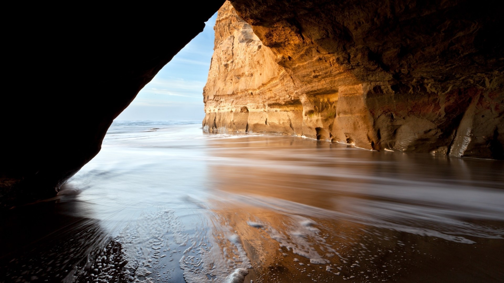 Cave entrance overlooking a beach with ocean waves HD Wallpaper