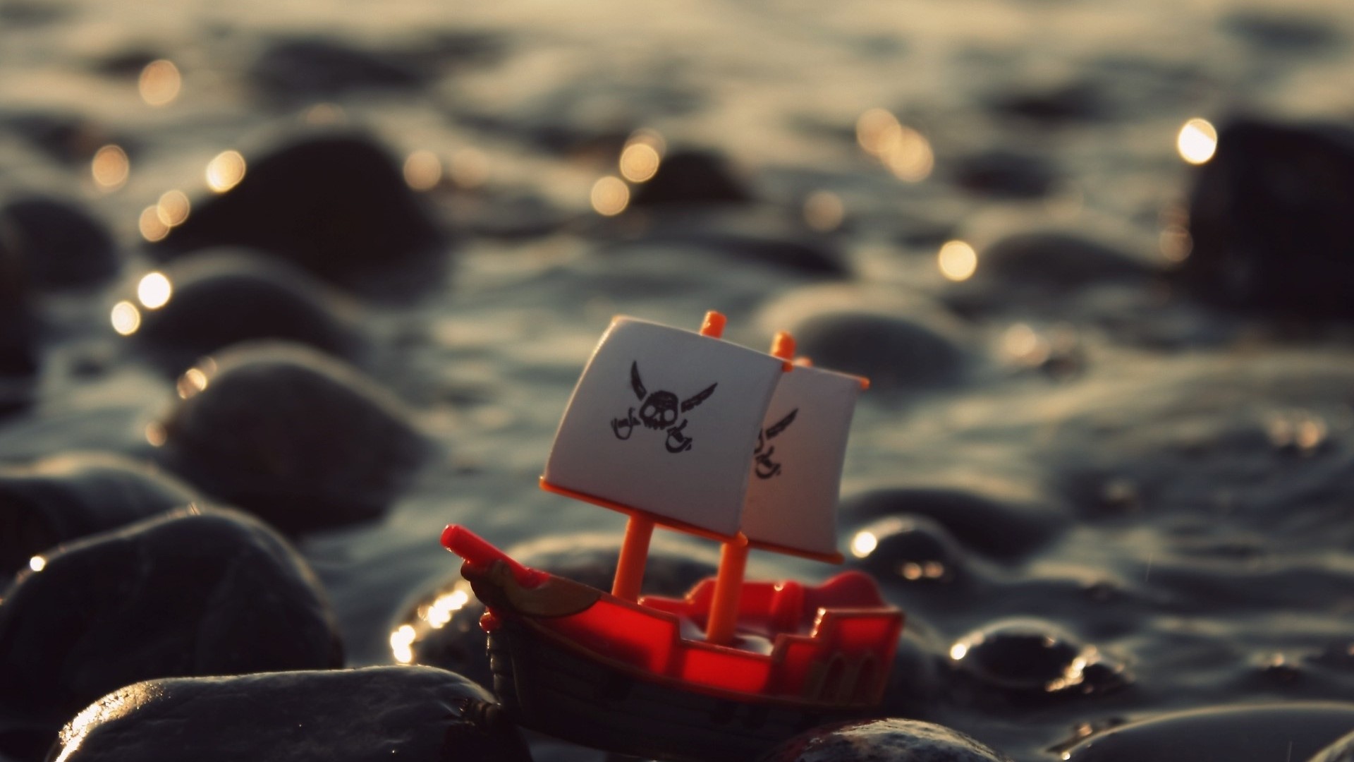 Toy pirate ship with skull and crossbones sails on rocks HD Wallpaper