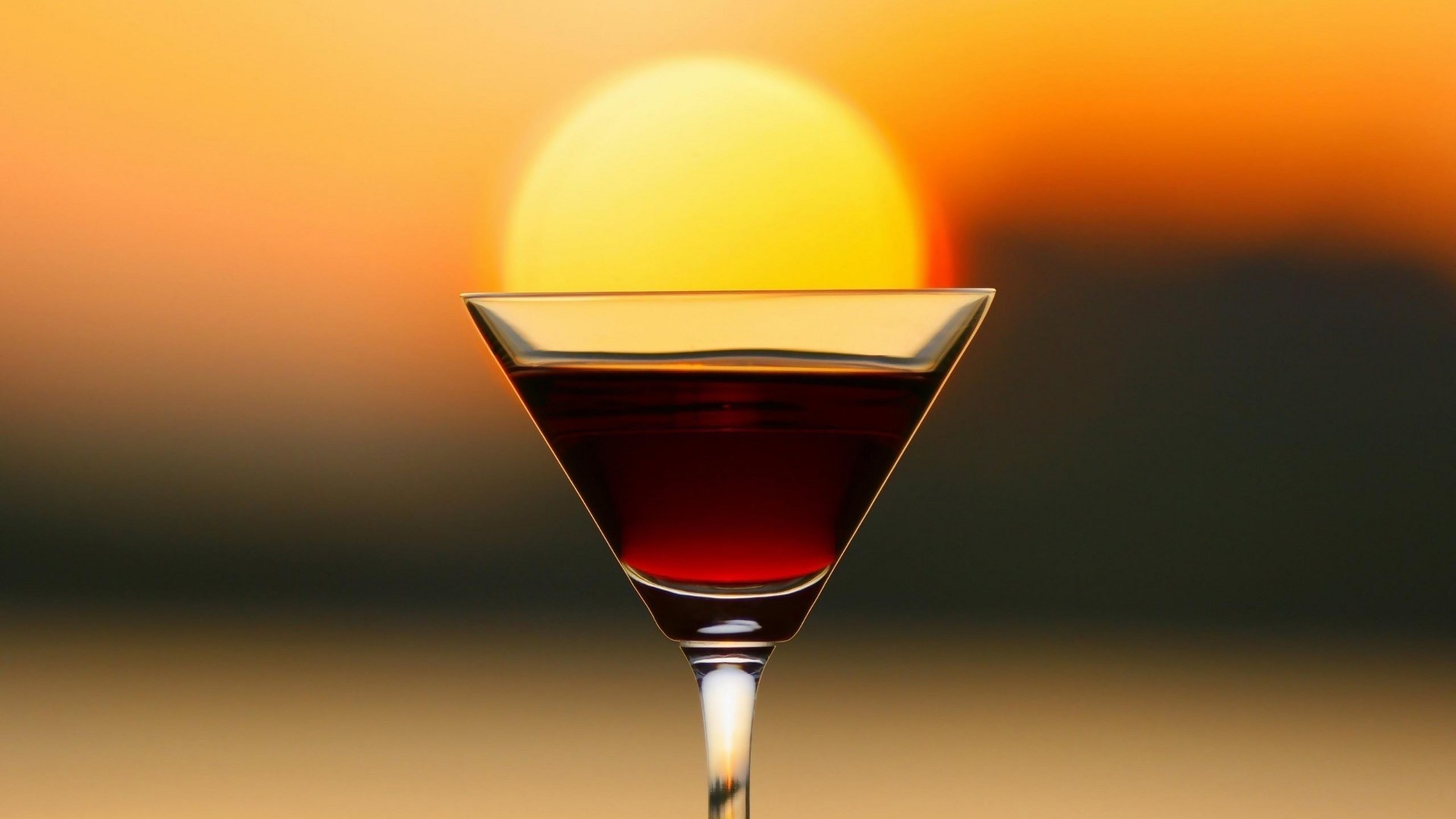 Cocktail glass with red liquid at sunset HD Wallpaper