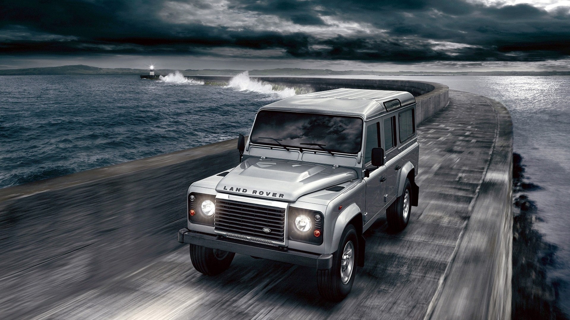 2012 Land Rover Defender driving on a coastal road HD Wallpaper