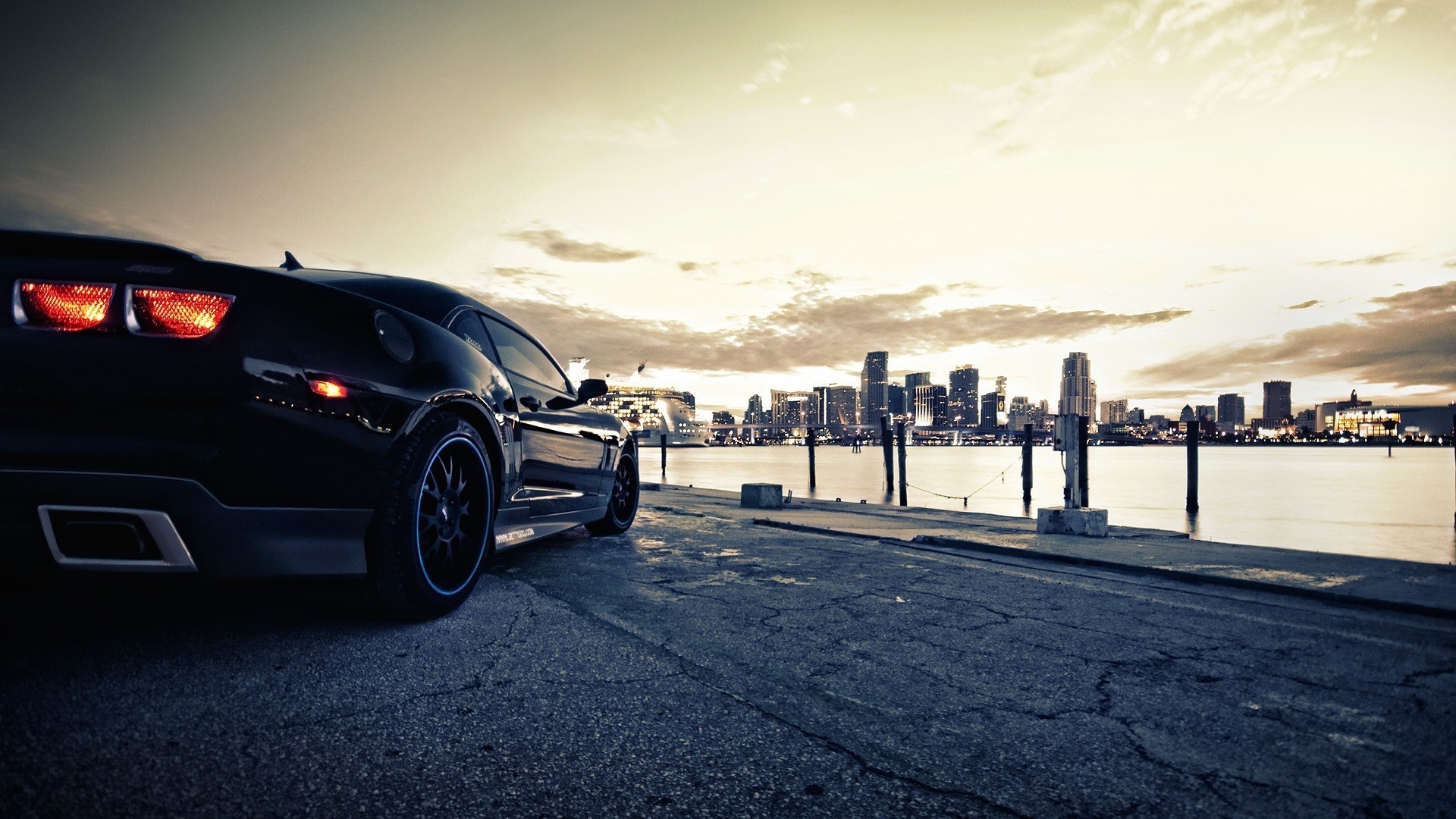 Black Chevrolet Camaro parked by a city skyline at dusk HD Wallpaper