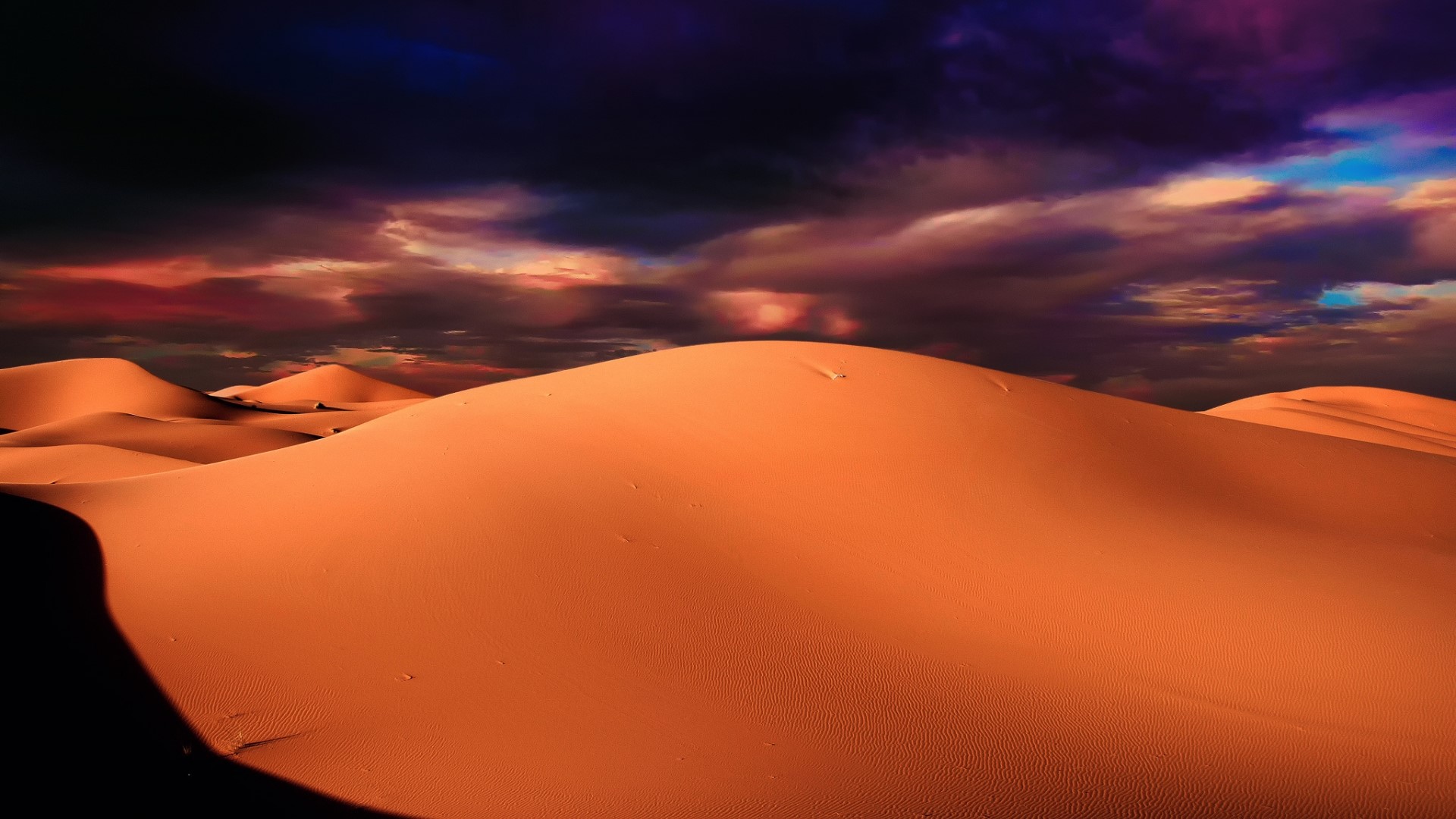 Desert sand dunes under a dramatic sky HD Wallpaper