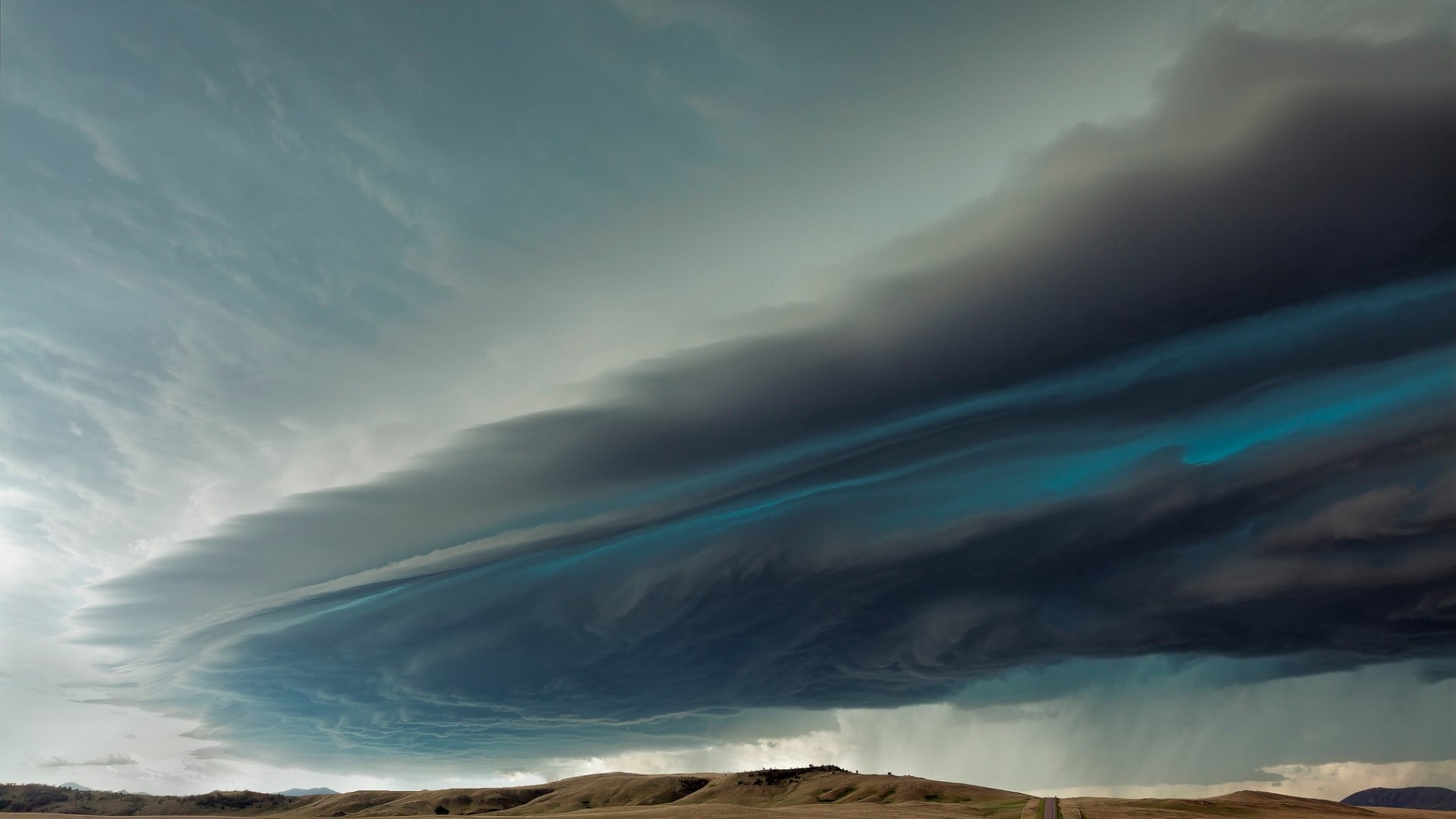 Dramatic storm clouds over rolling hills HD Wallpaper