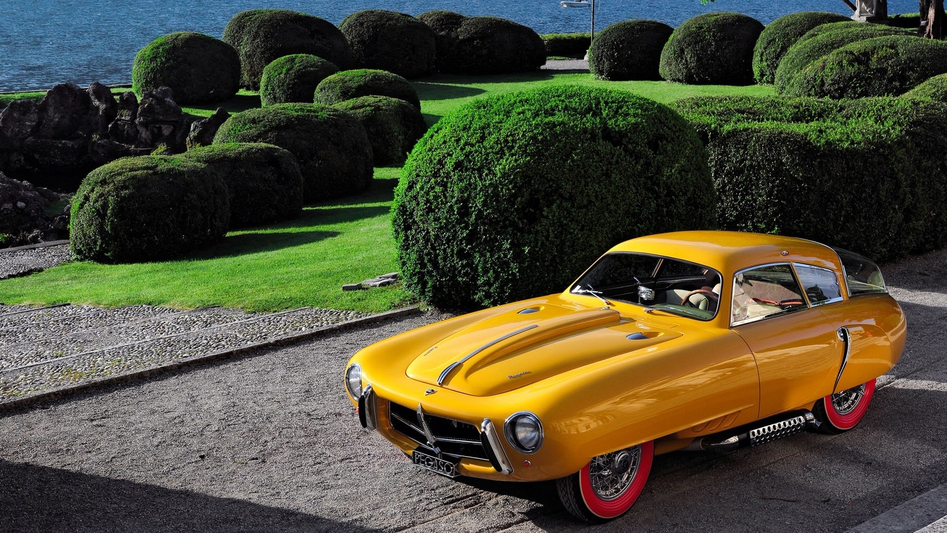 Yellow Pegaso Z 102 by a lake with manicured bushes HD Wallpaper