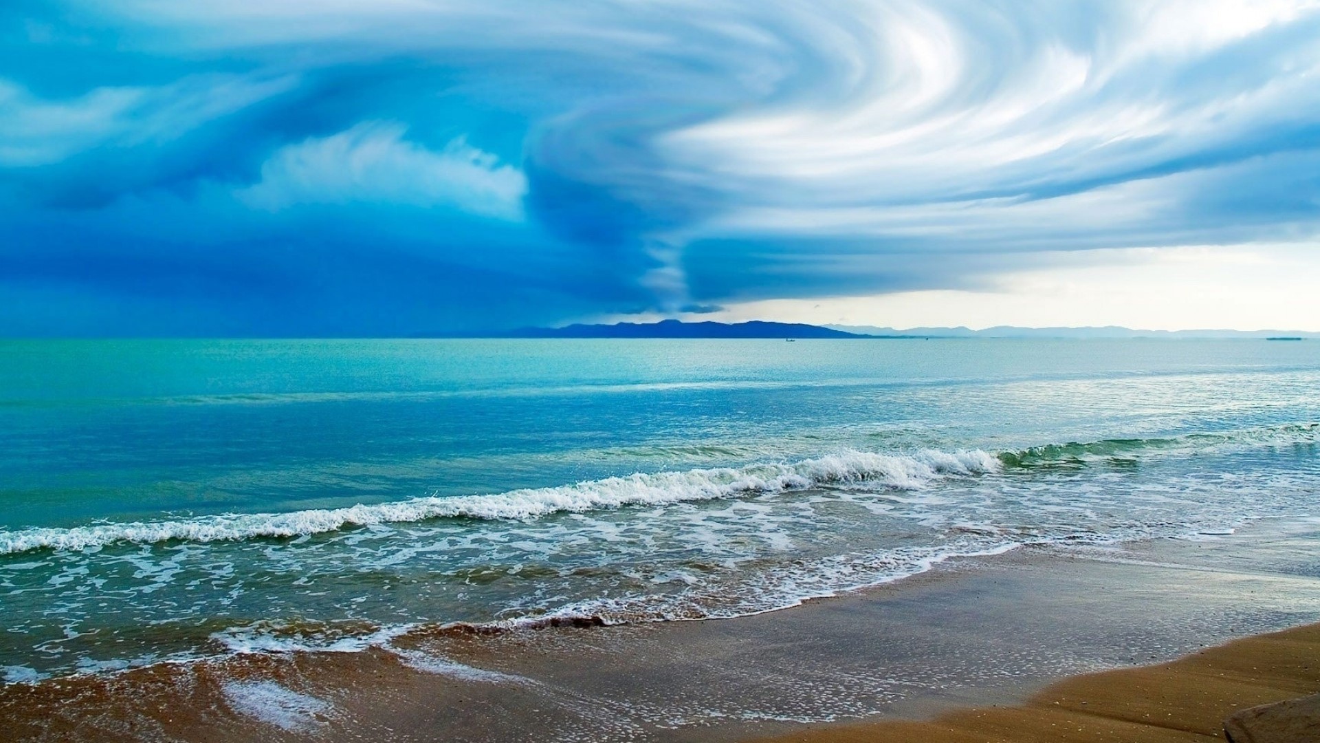 Ocean waves crash on a sandy shore under dramatic clouds HD Wallpaper