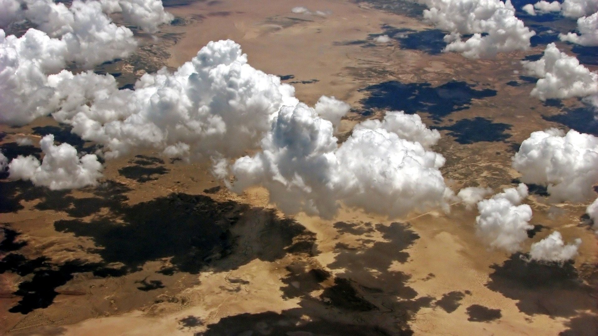 Clouds casting shadows over desert landscape from above HD Wallpaper