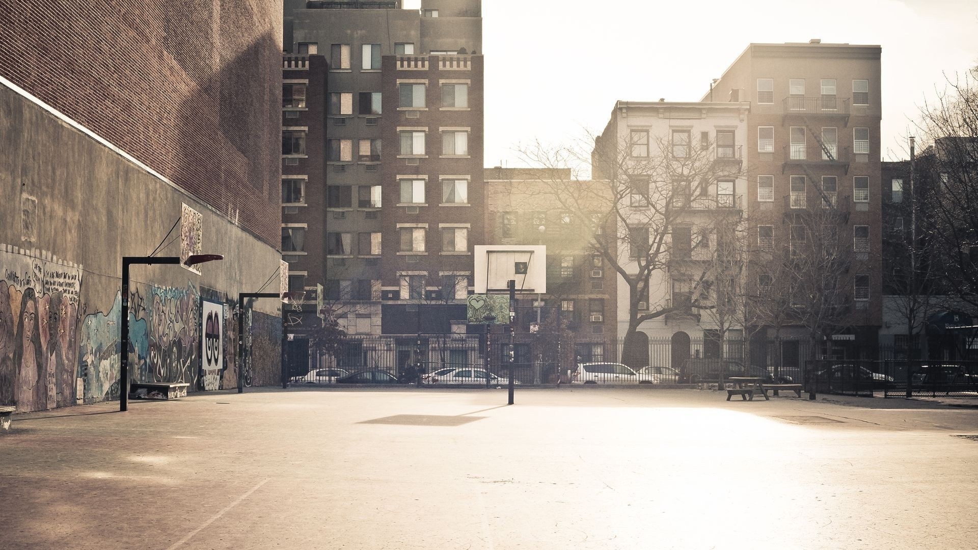 Basketball court in a city with buildings and murals HD Wallpaper