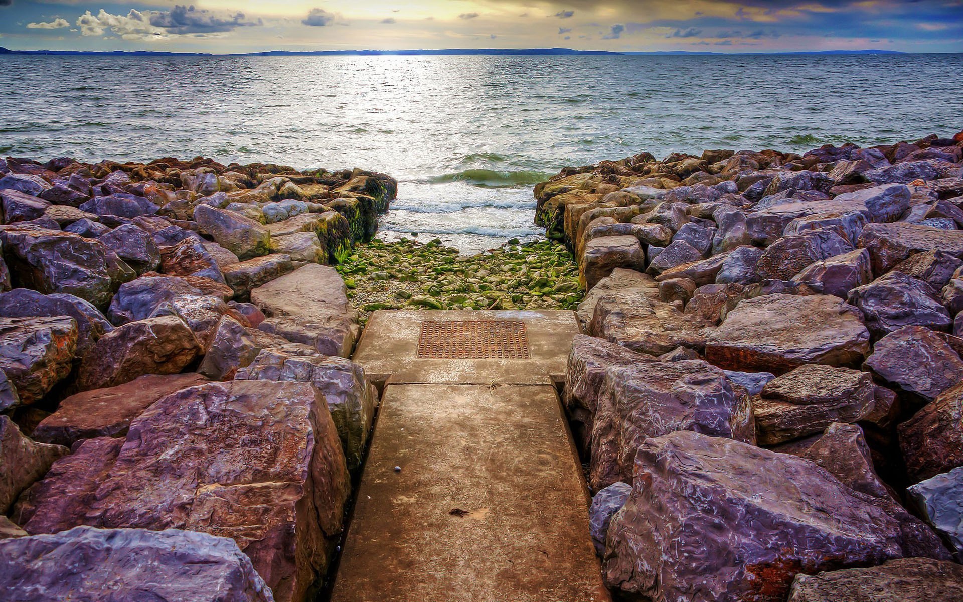 Rocky shoreline with a path leading to the sea HD Wallpaper