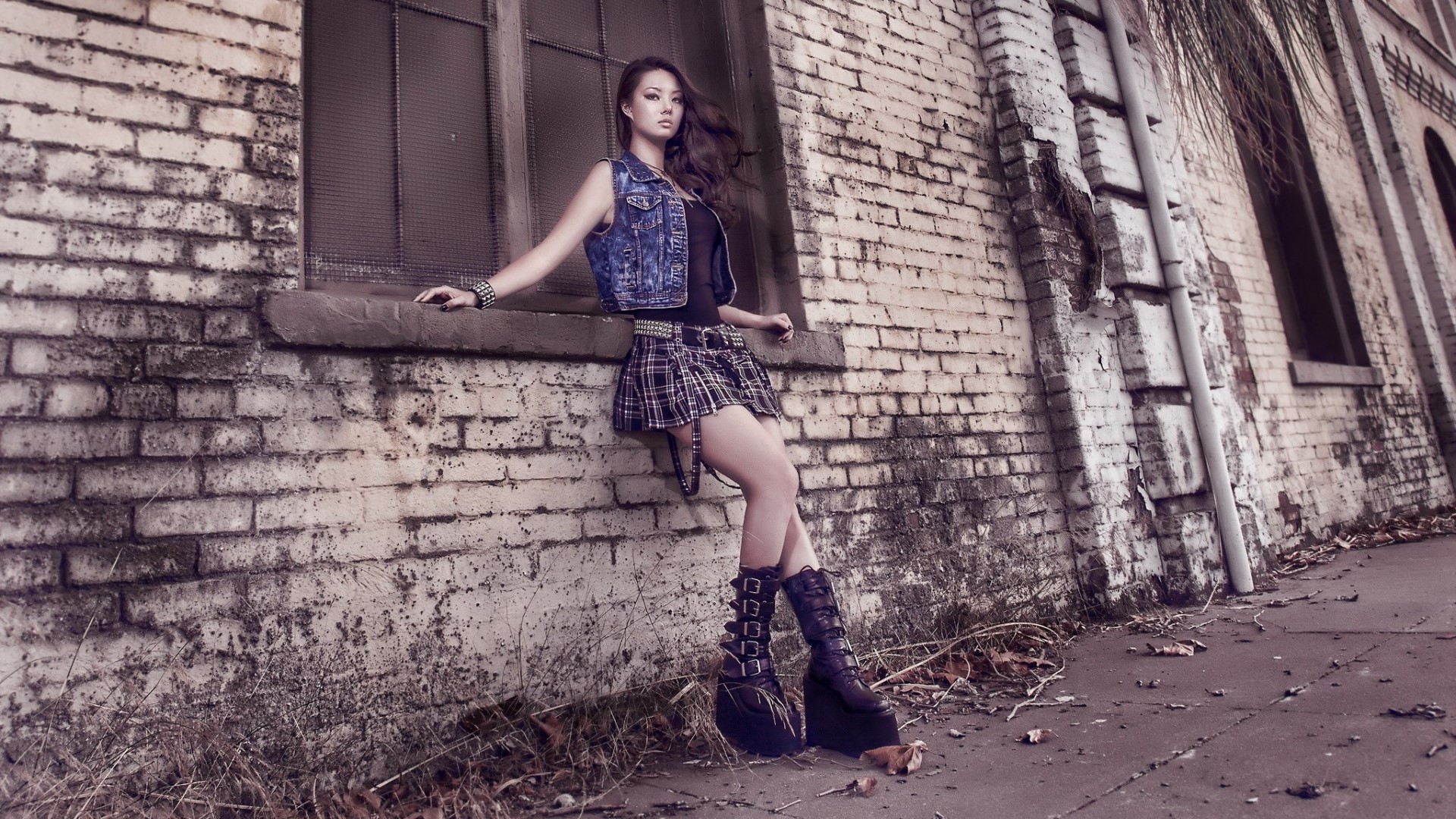 Girl in denim vest and plaid skirt leaning on brick wall HD Wallpaper