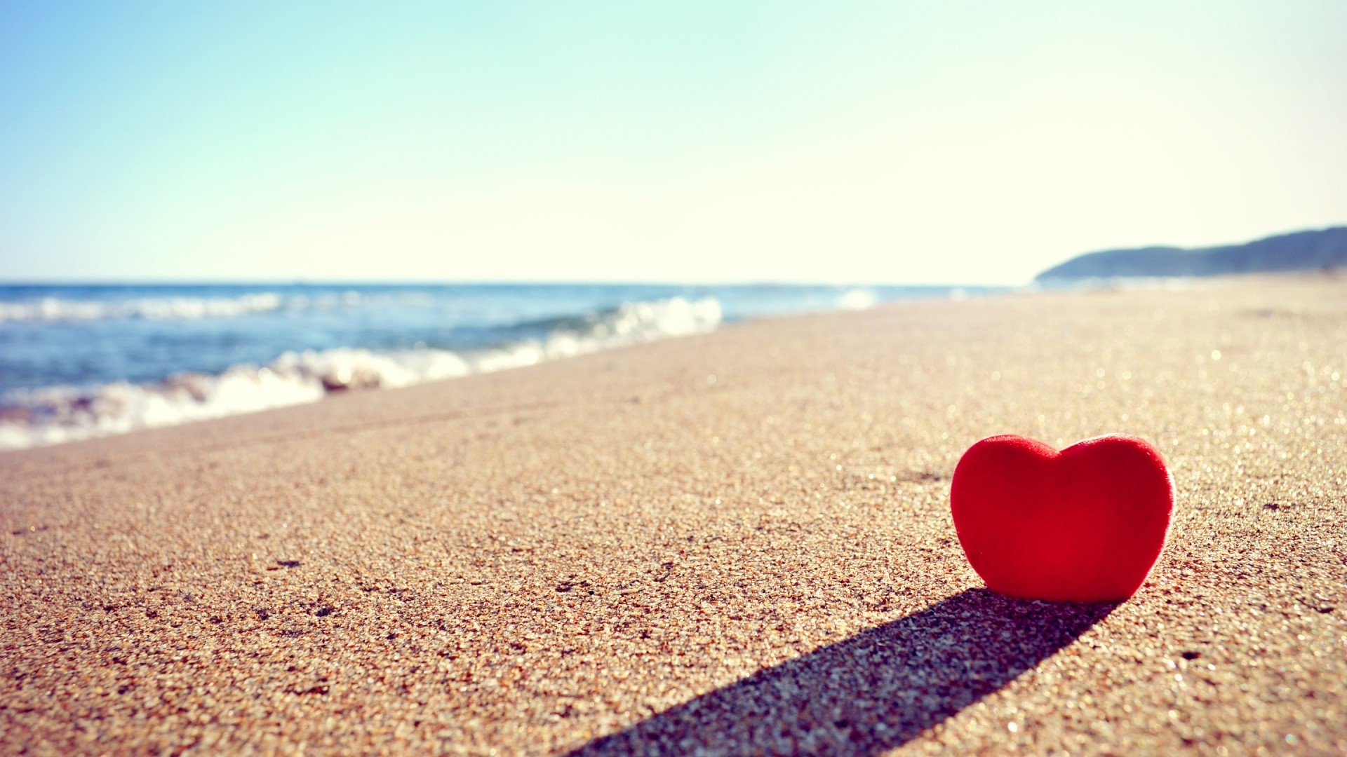 Red heart on a sandy beach with ocean waves HD Wallpaper