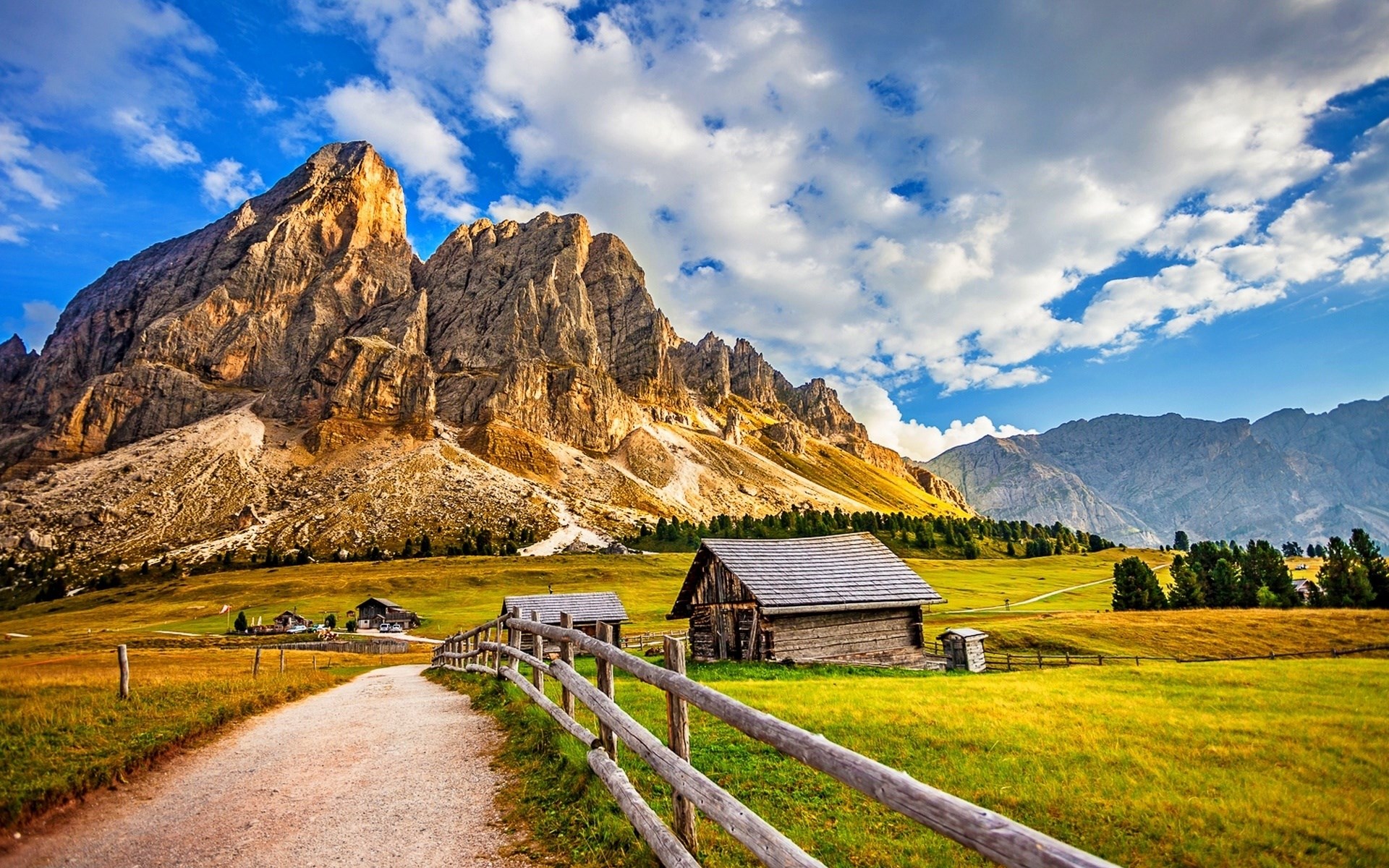 Mountain landscape with wooden cabins and a dirt path HD Wallpaper