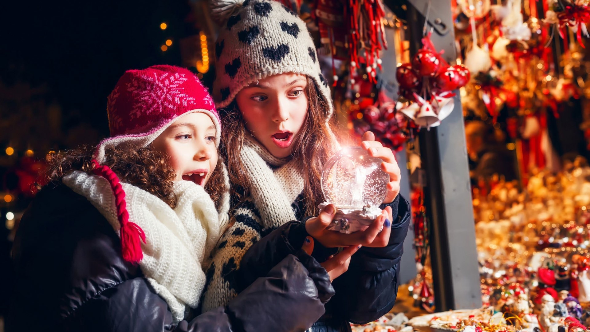 Two girls looking at a snow globe at a Christmas market HD Wallpaper