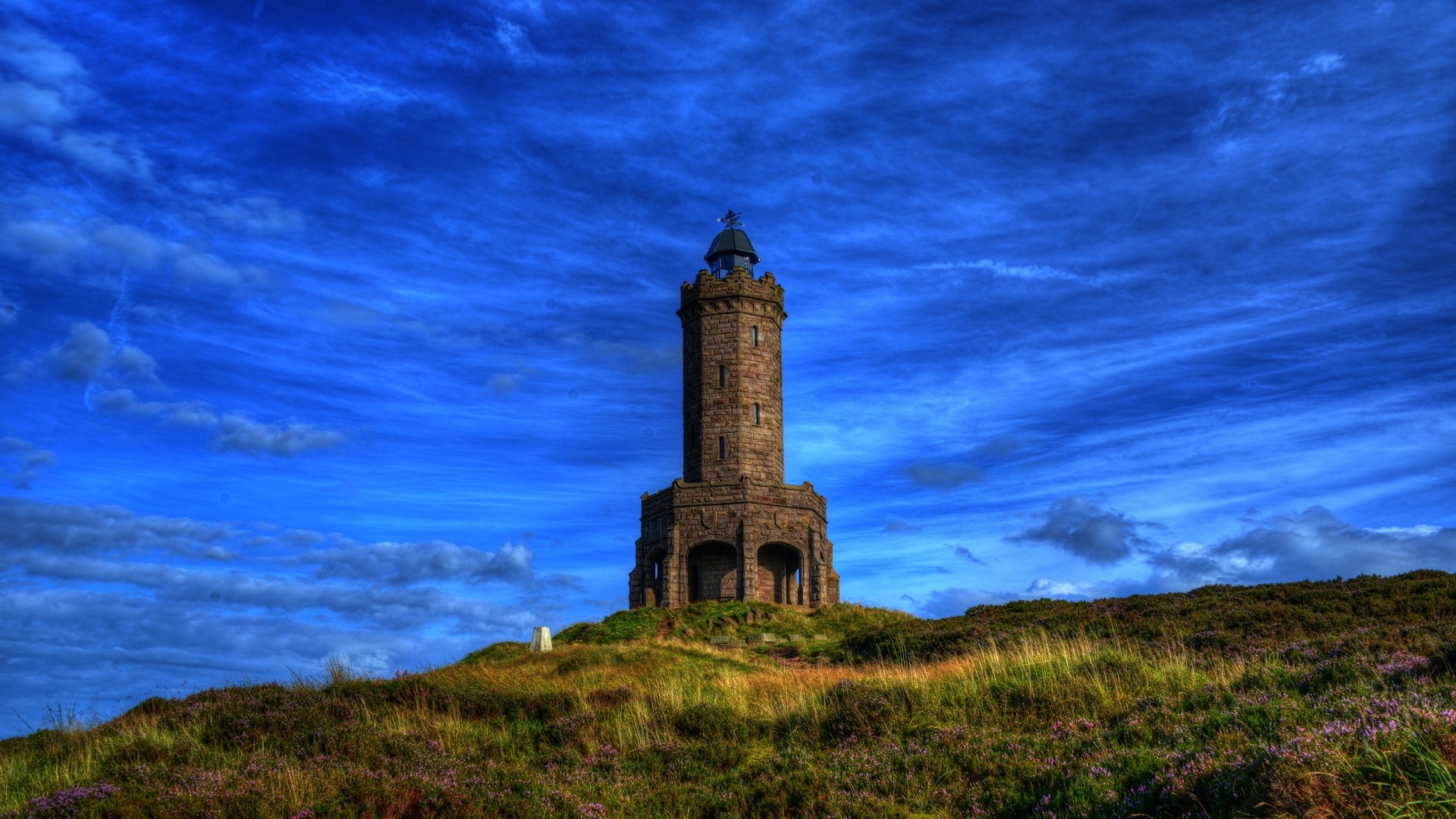 Stone tower on a grassy hill under a blue sky HD Wallpaper
