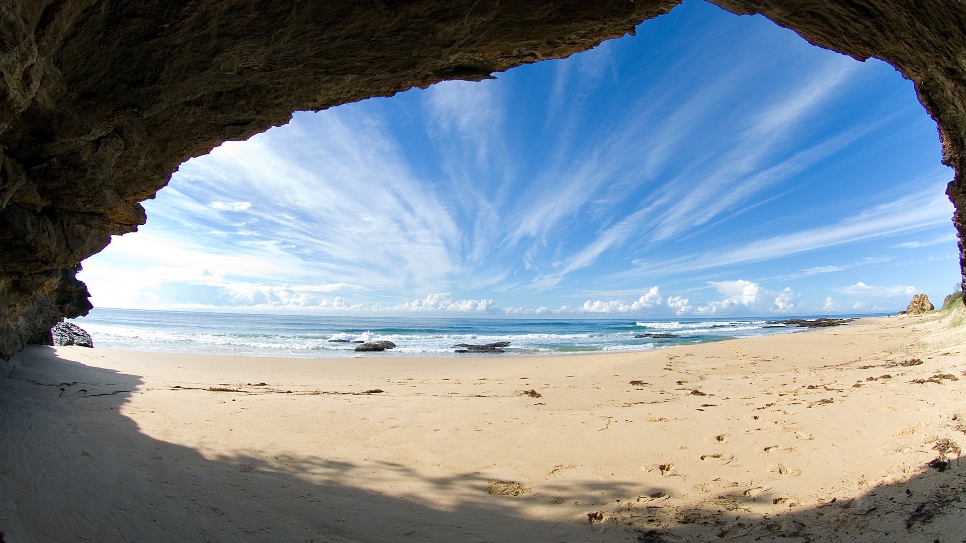 Cave entrance overlooking a sandy beach and ocean HD Wallpaper