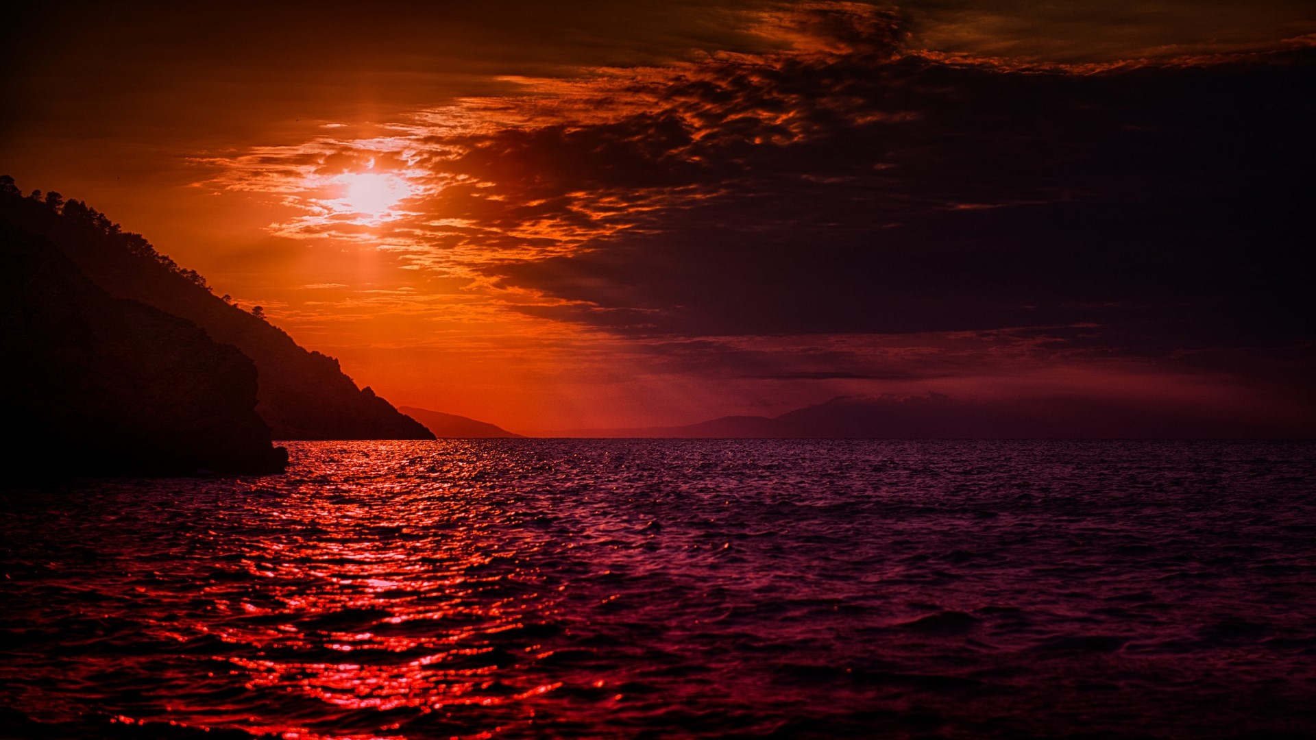 Sunset over the ocean with a mountain silhouette HD Wallpaper