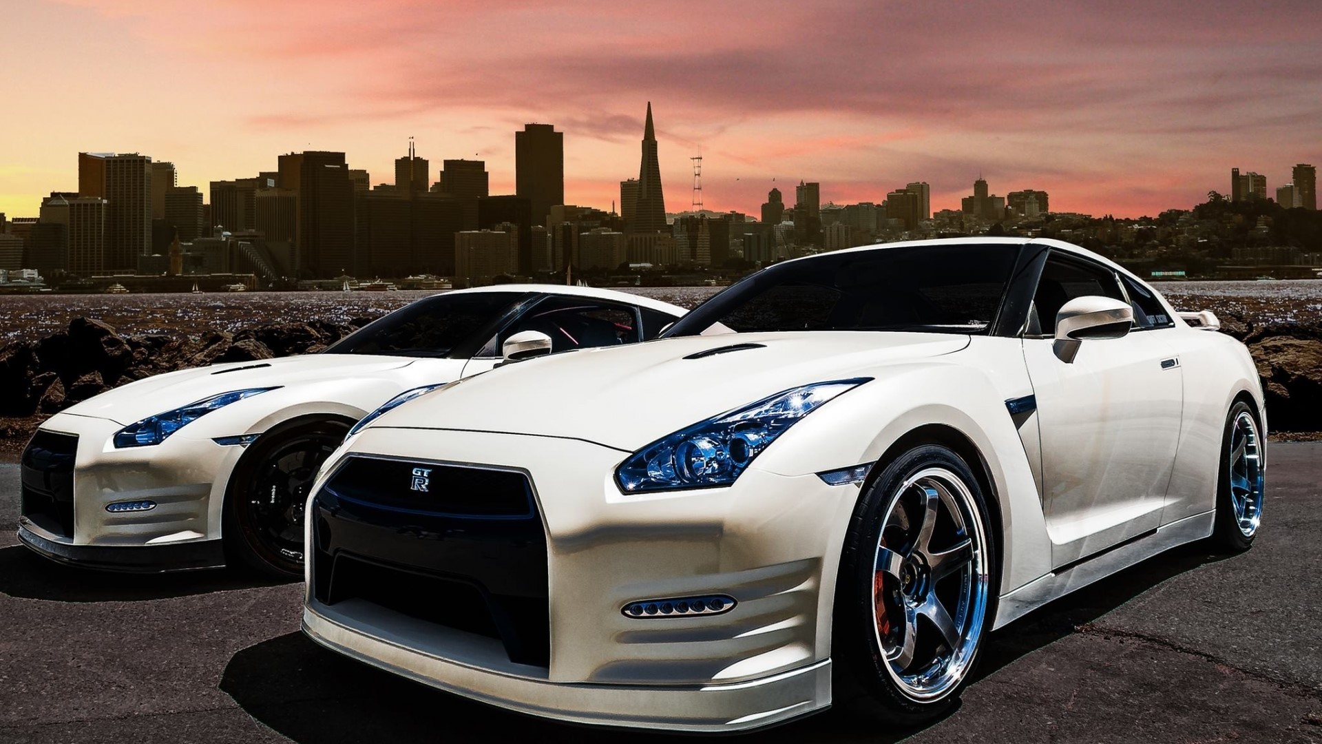 Two white Nissan GT-R cars in front of a city skyline HD Wallpaper
