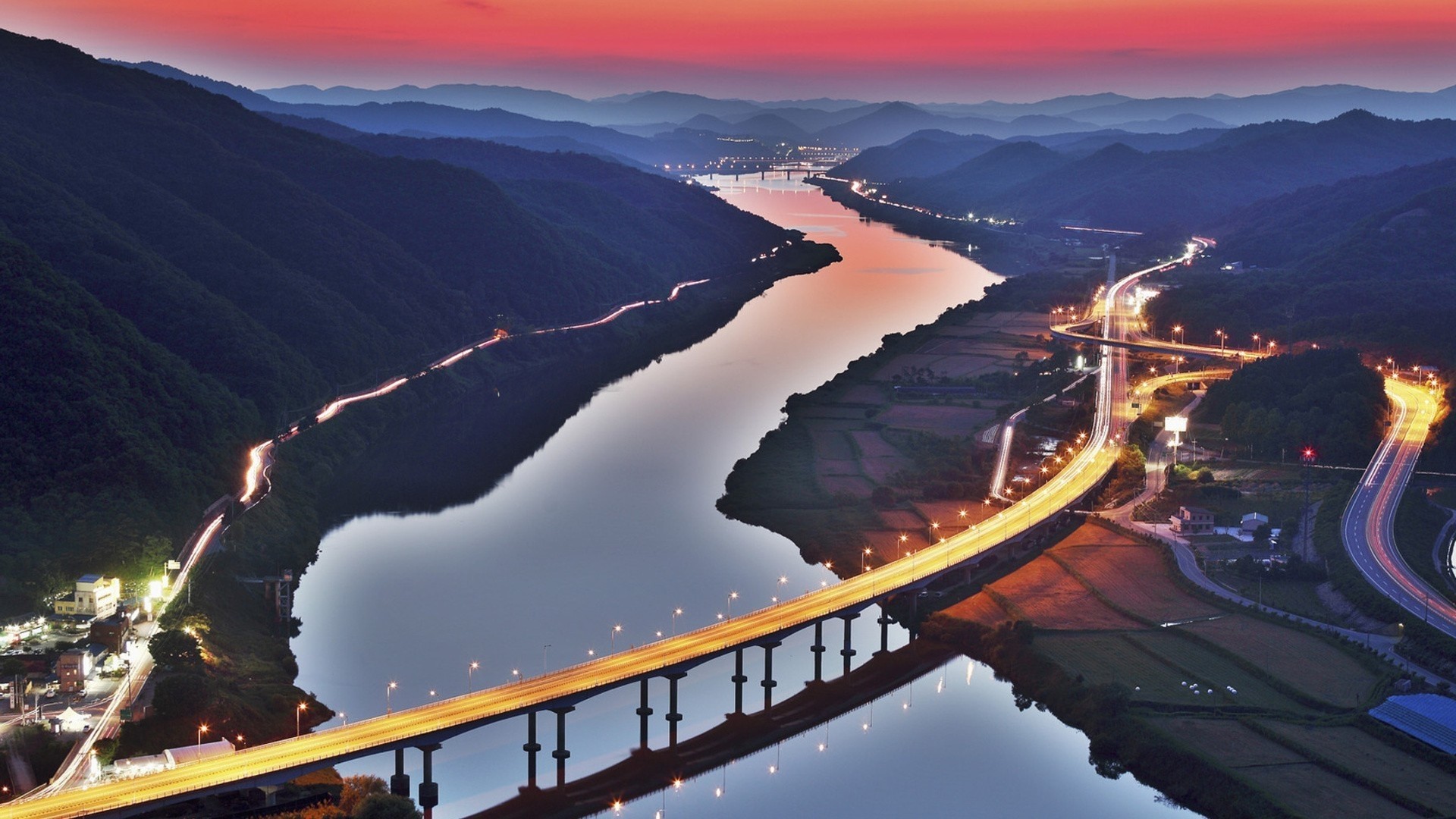 Bridge over river at dusk with mountains and lights HD Wallpaper