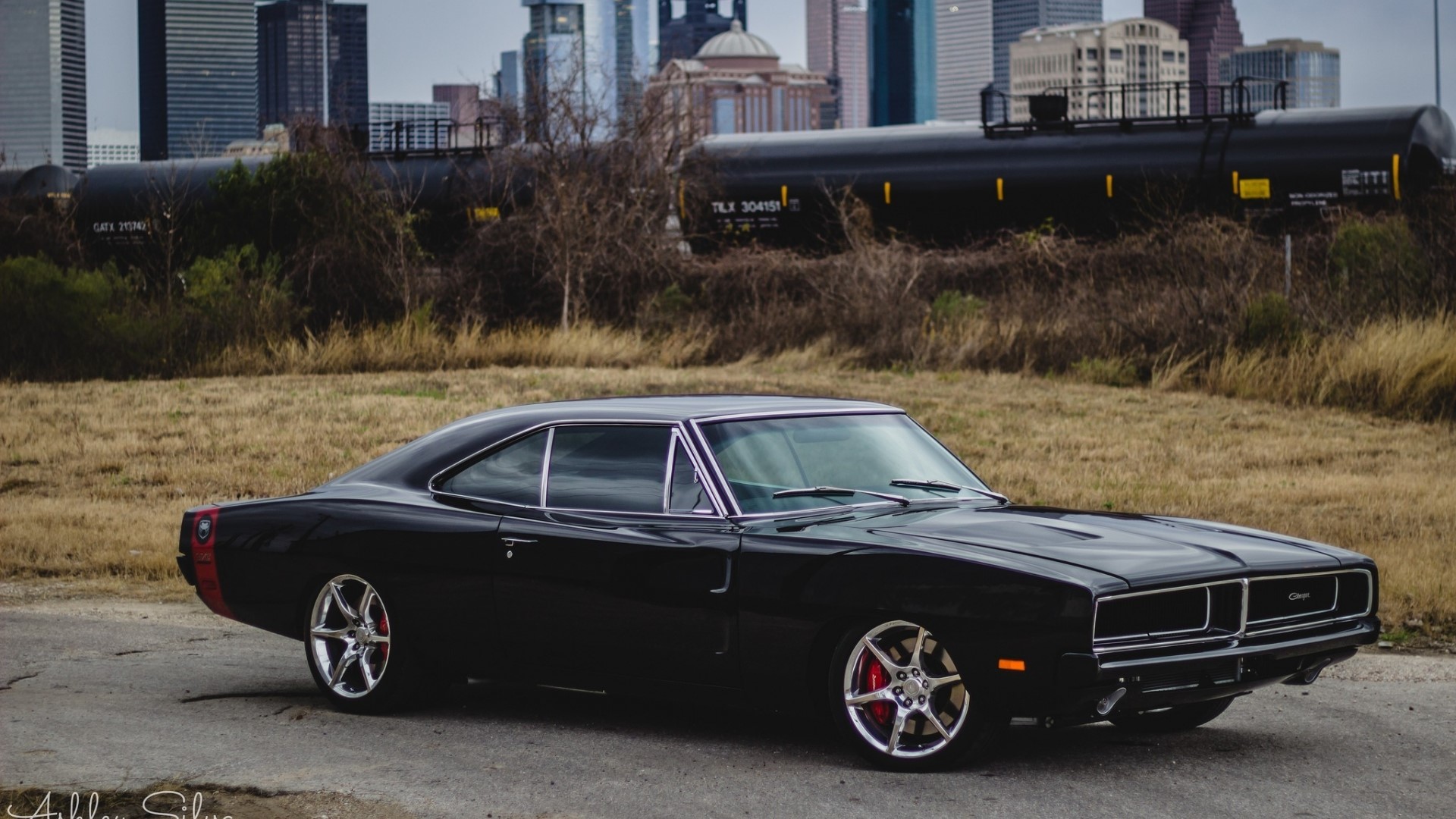Black Dodge Charger parked with city skyline and trains HD Wallpaper