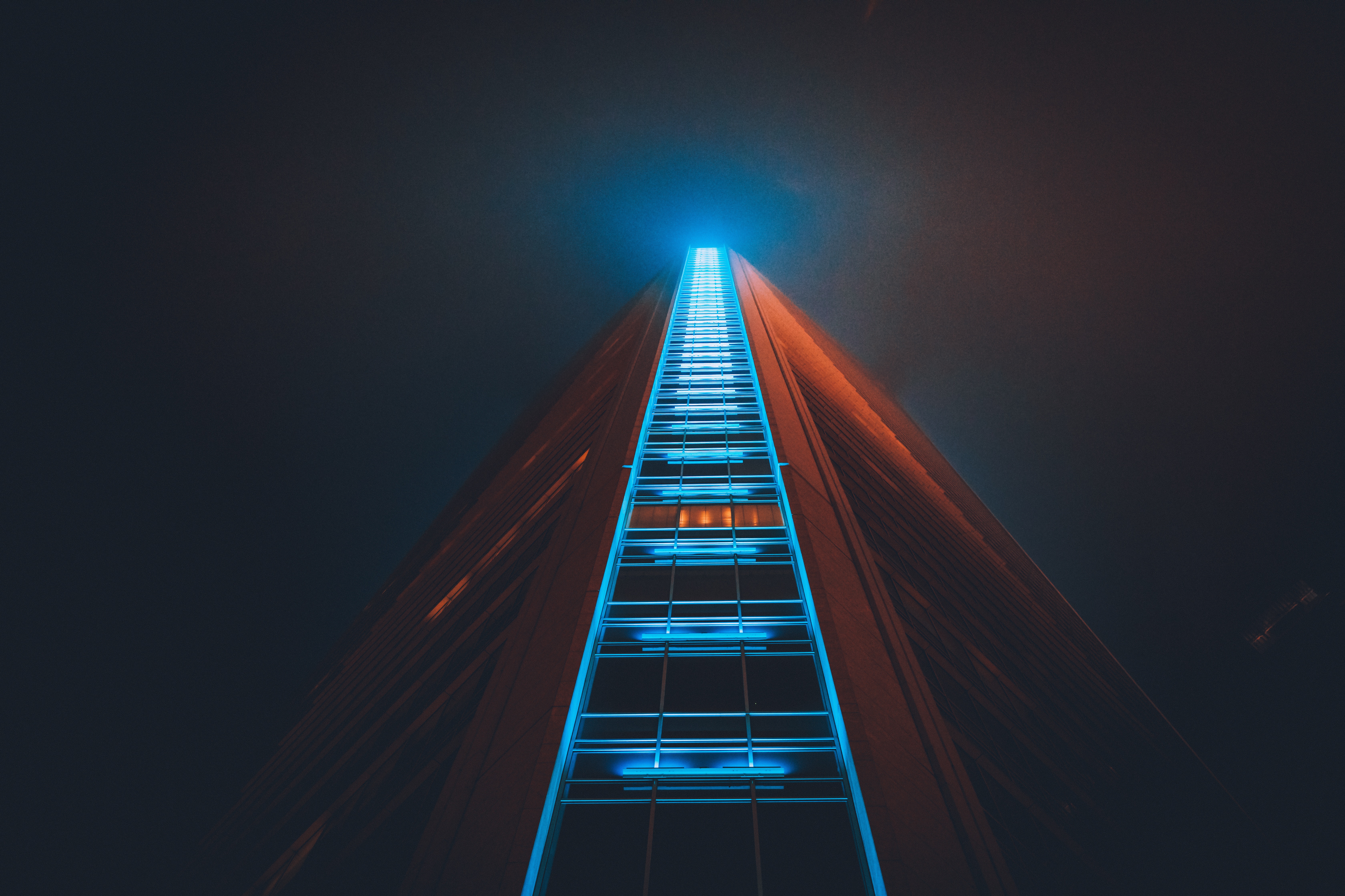 Skyscraper with blue and orange lights at night HD Wallpaper