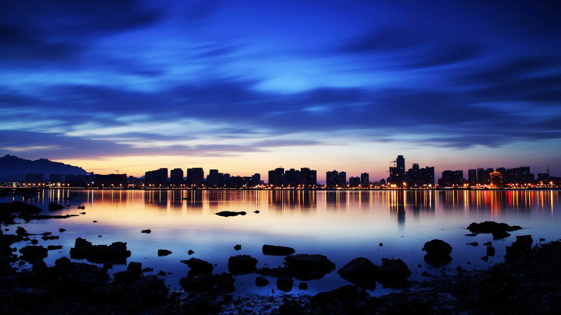 Sunset over a city skyline reflected in water HD Wallpaper