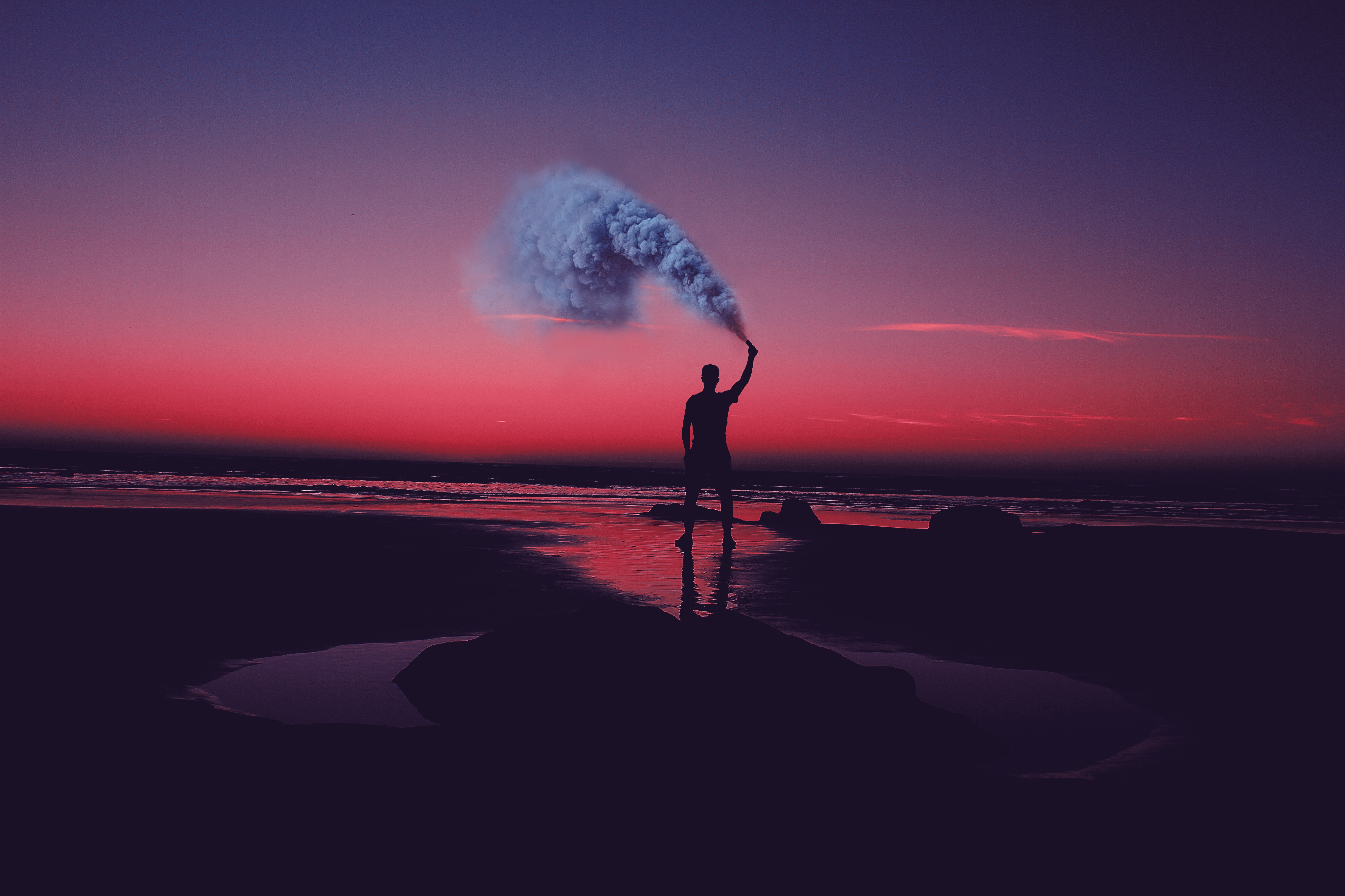 Silhouette of a person holding a smoke flare on a beach at sunset HD Wallpaper