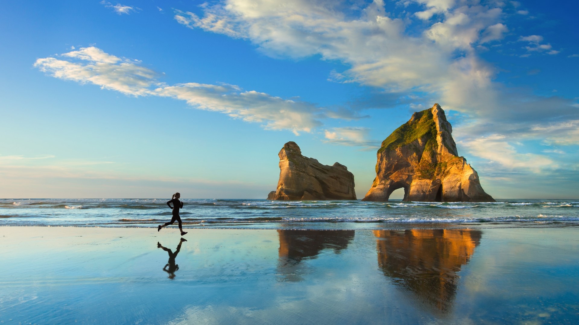 Person jogging on a beach with rock formations HD Wallpaper
