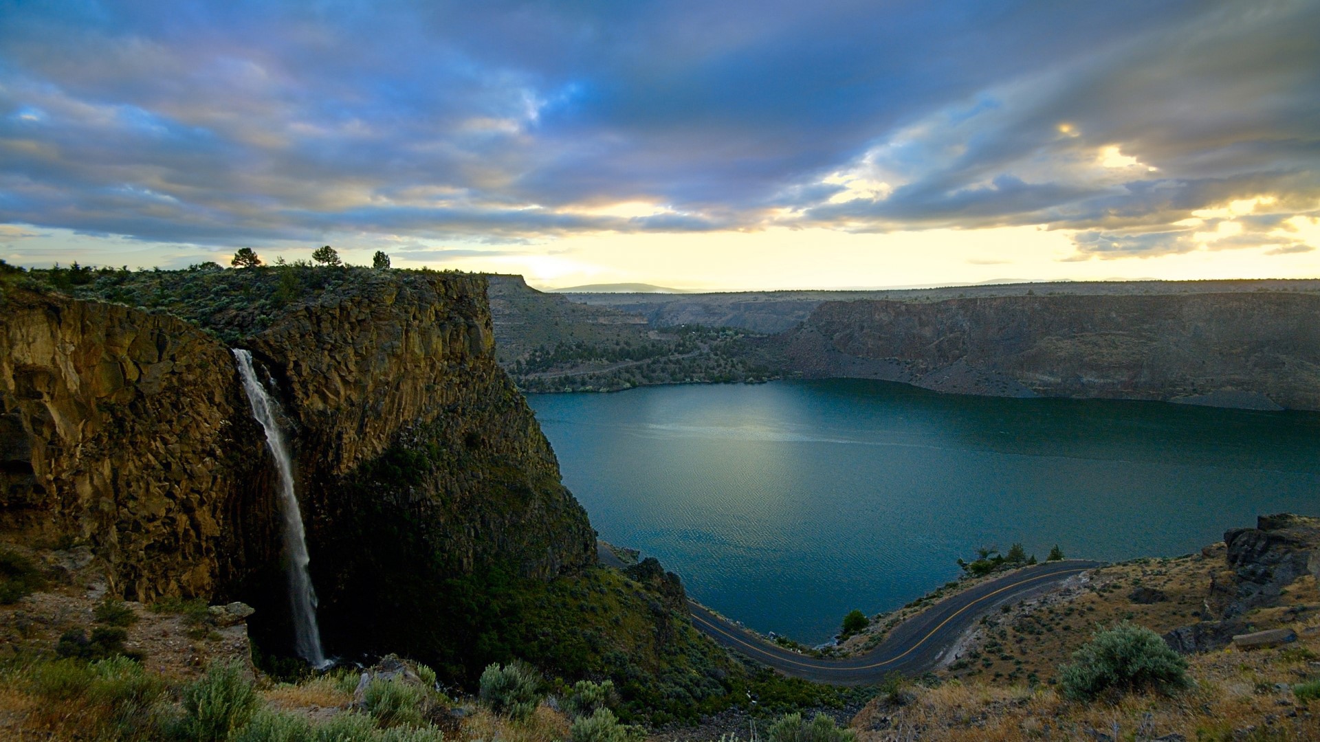 Waterfall cascading into a lake with a road HD Wallpaper