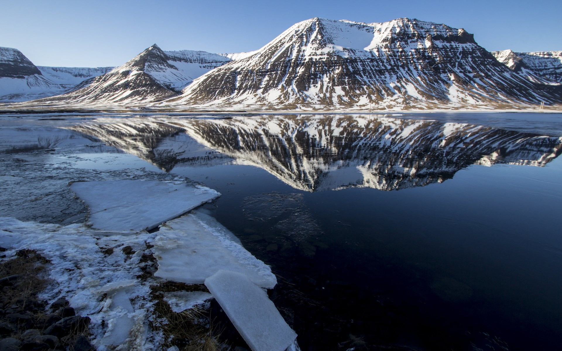 Snow-covered mountains reflected in a calm lake with ice HD Wallpaper