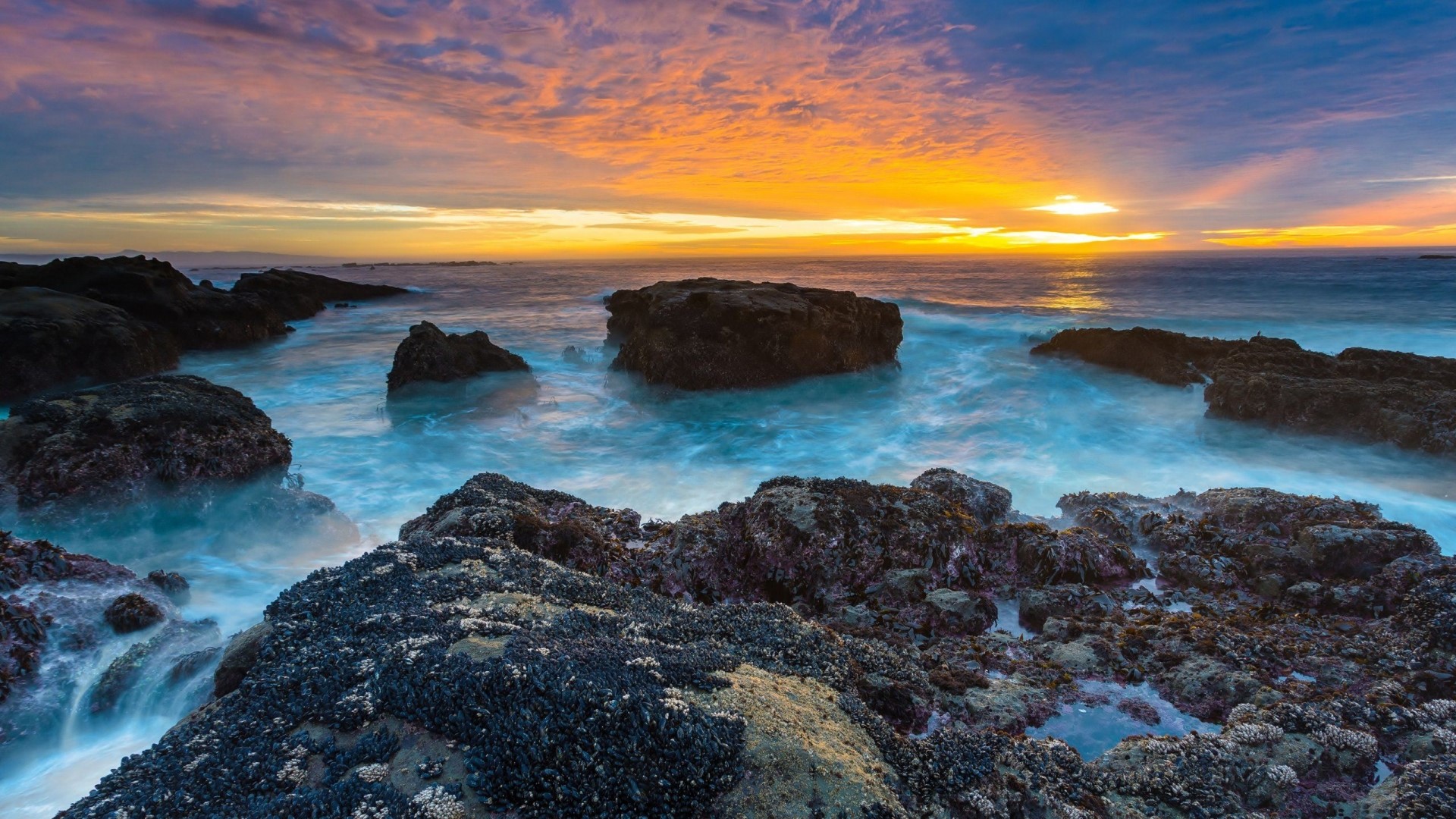 Sunset over rocky sea coast with crashing waves HD Wallpaper