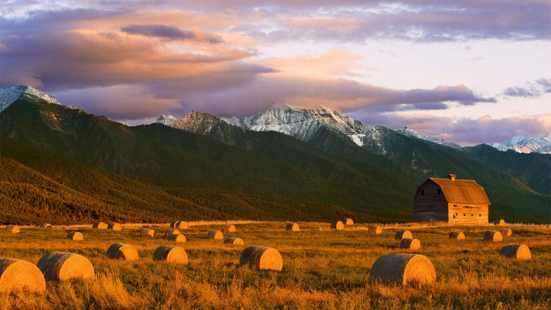 Barn and hay bales in a mountain field at sunset HD Wallpaper