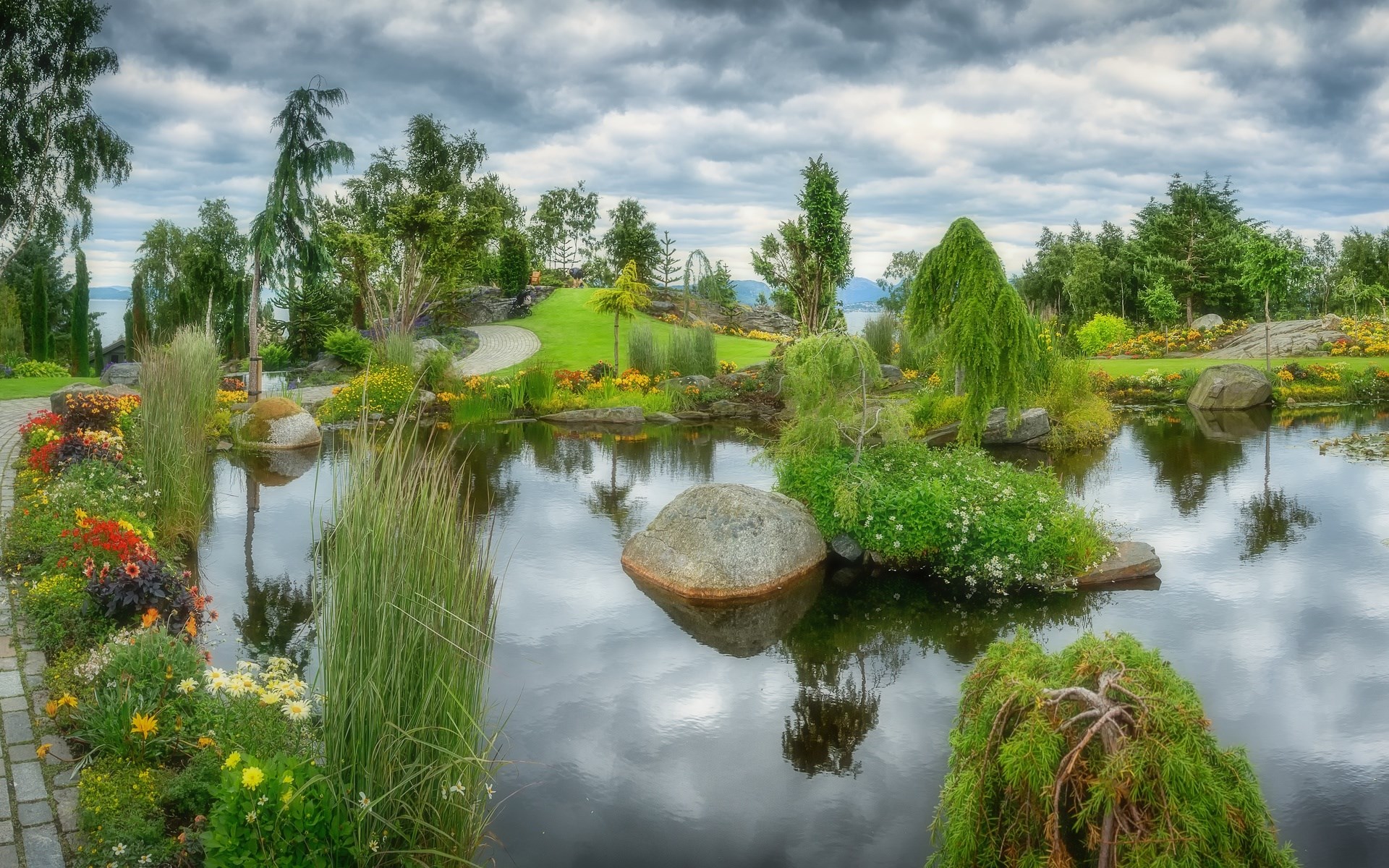 A tranquil garden pond with colorful flowers and trees HD Wallpaper