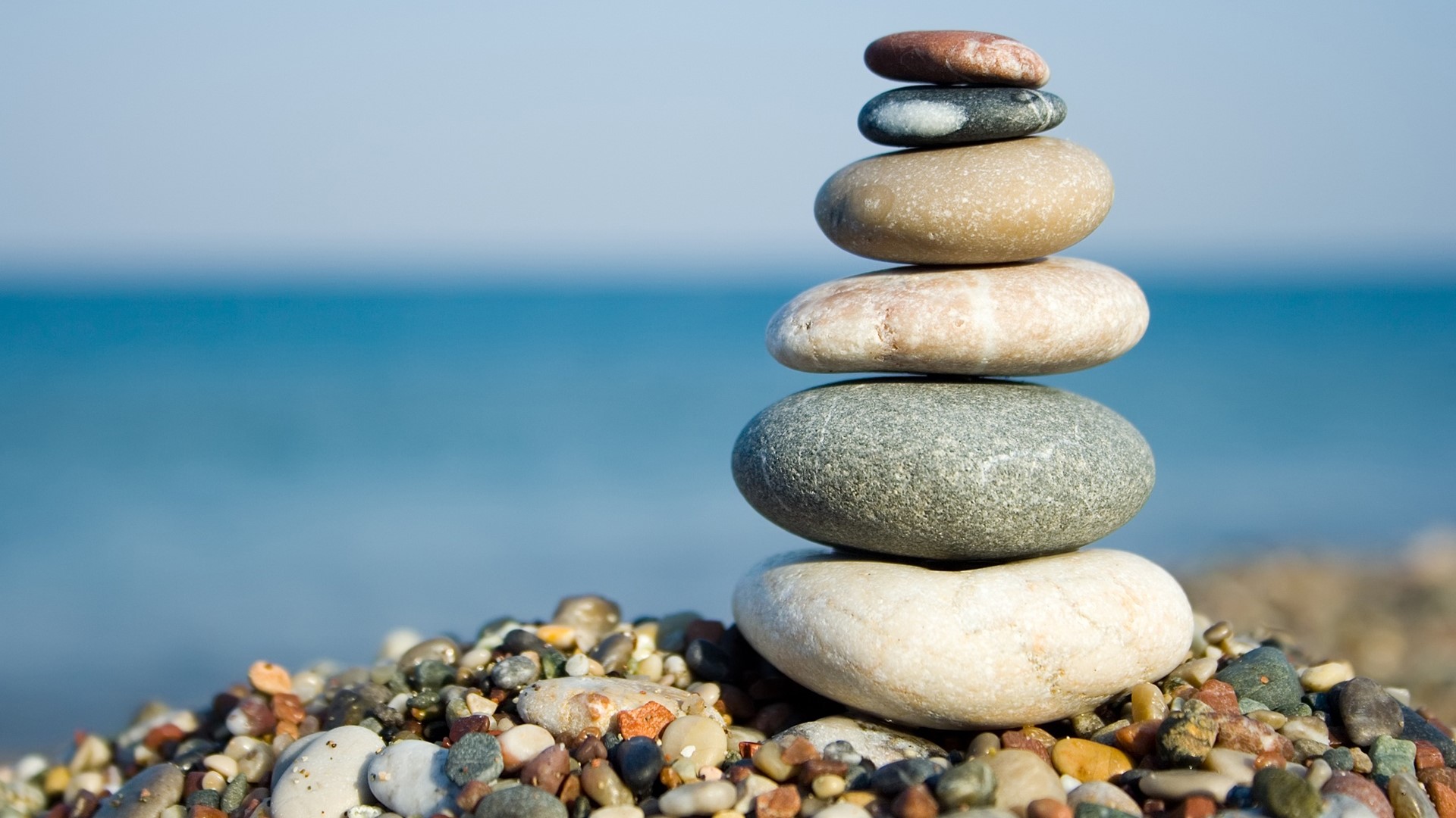 Stack of stones on a beach with ocean background HD Wallpaper