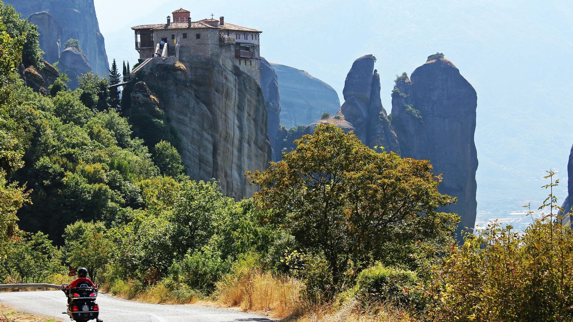 Monastery on a cliff in Meteora, Greece with a motorcyclist HD Wallpaper