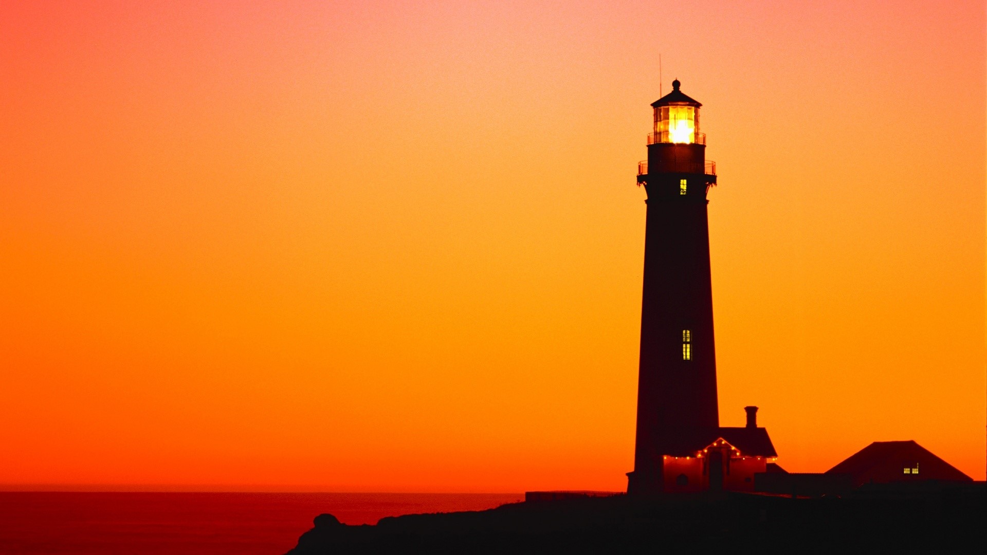 Lighthouse silhouette against a vibrant sunset HD Wallpaper