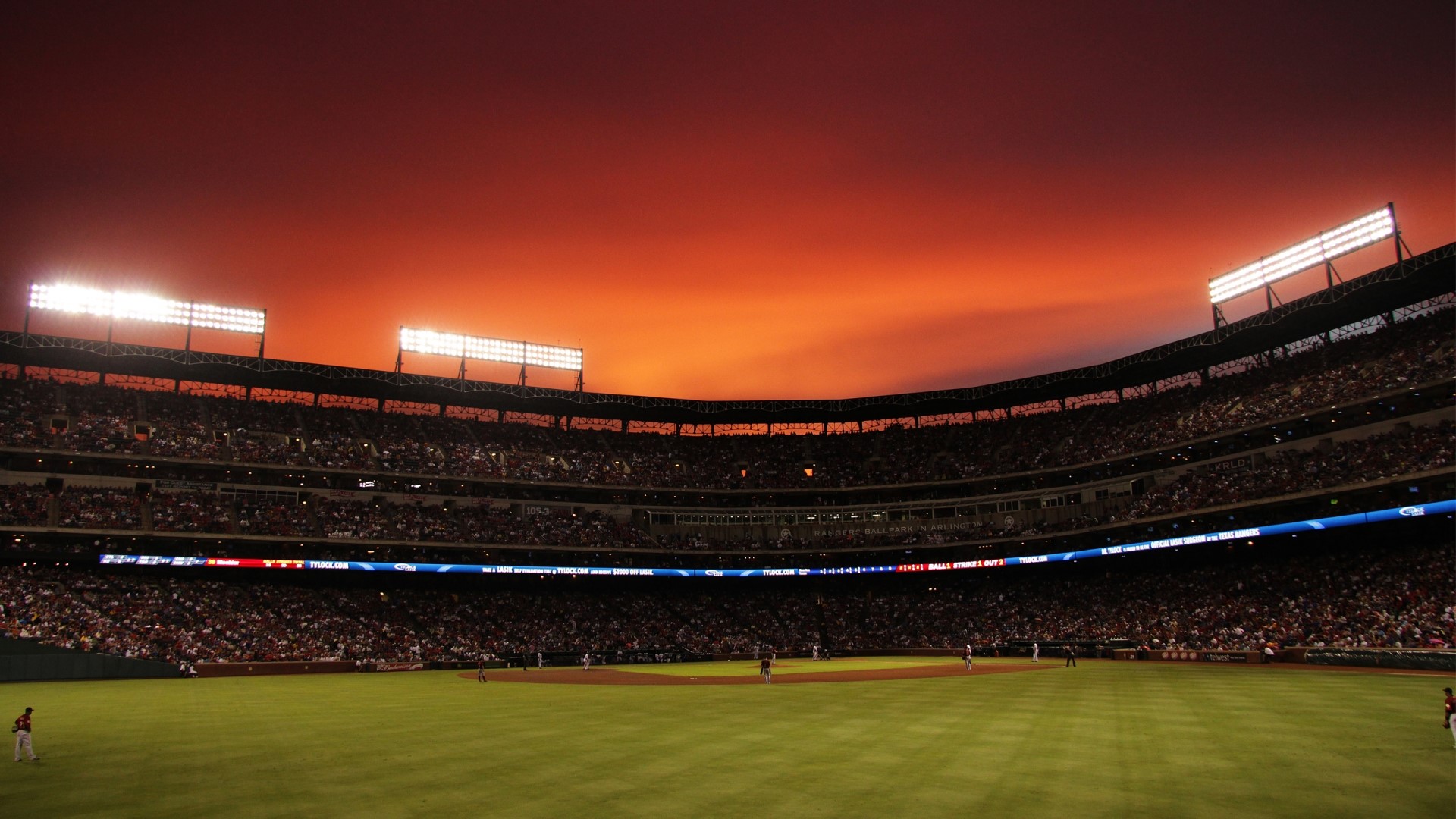 Baseball stadium at sunset with Texas Rangers and Houston Astros logos HD Wallpaper