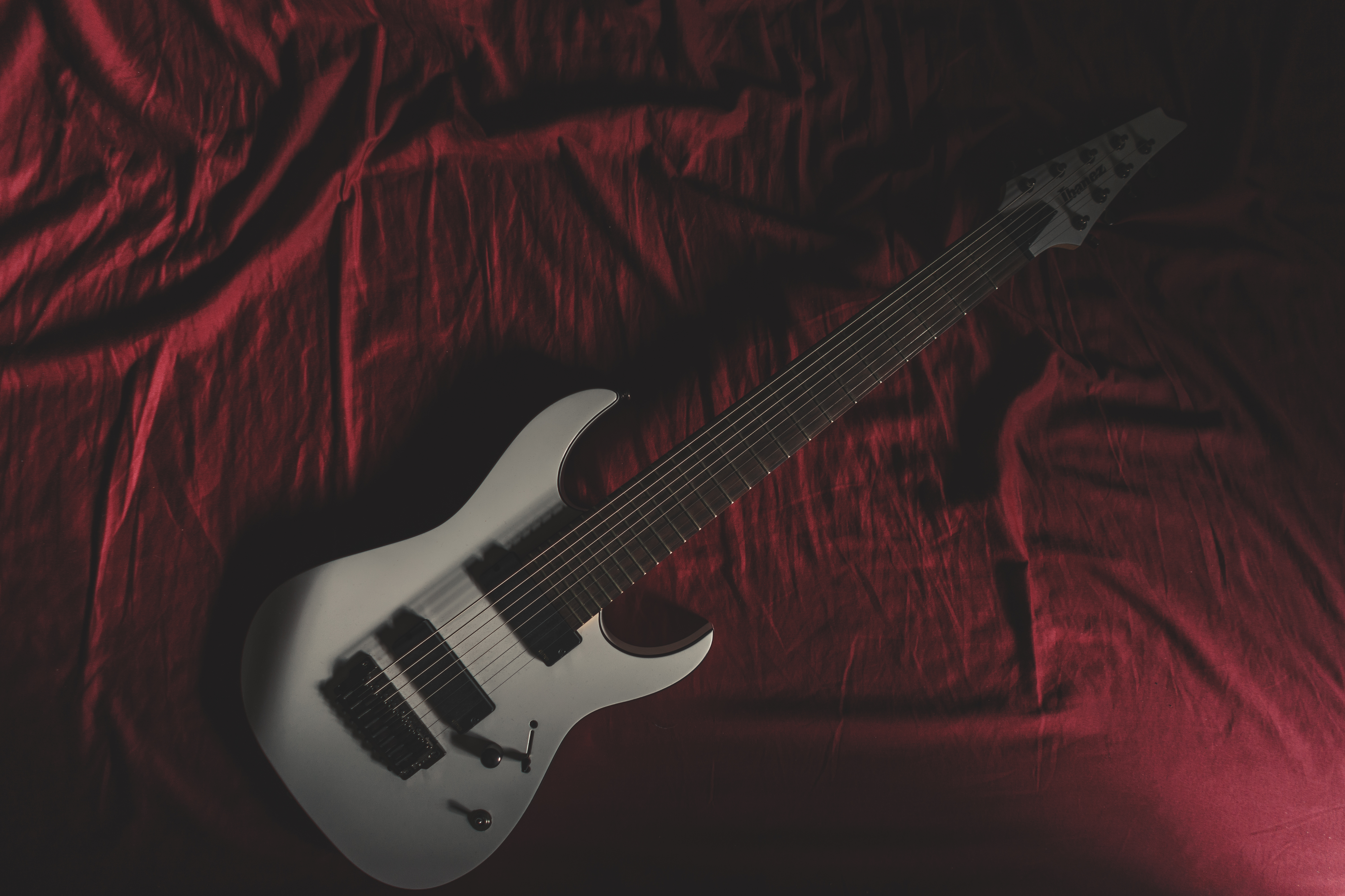 White 8-string electric guitar on red fabric HD Wallpaper